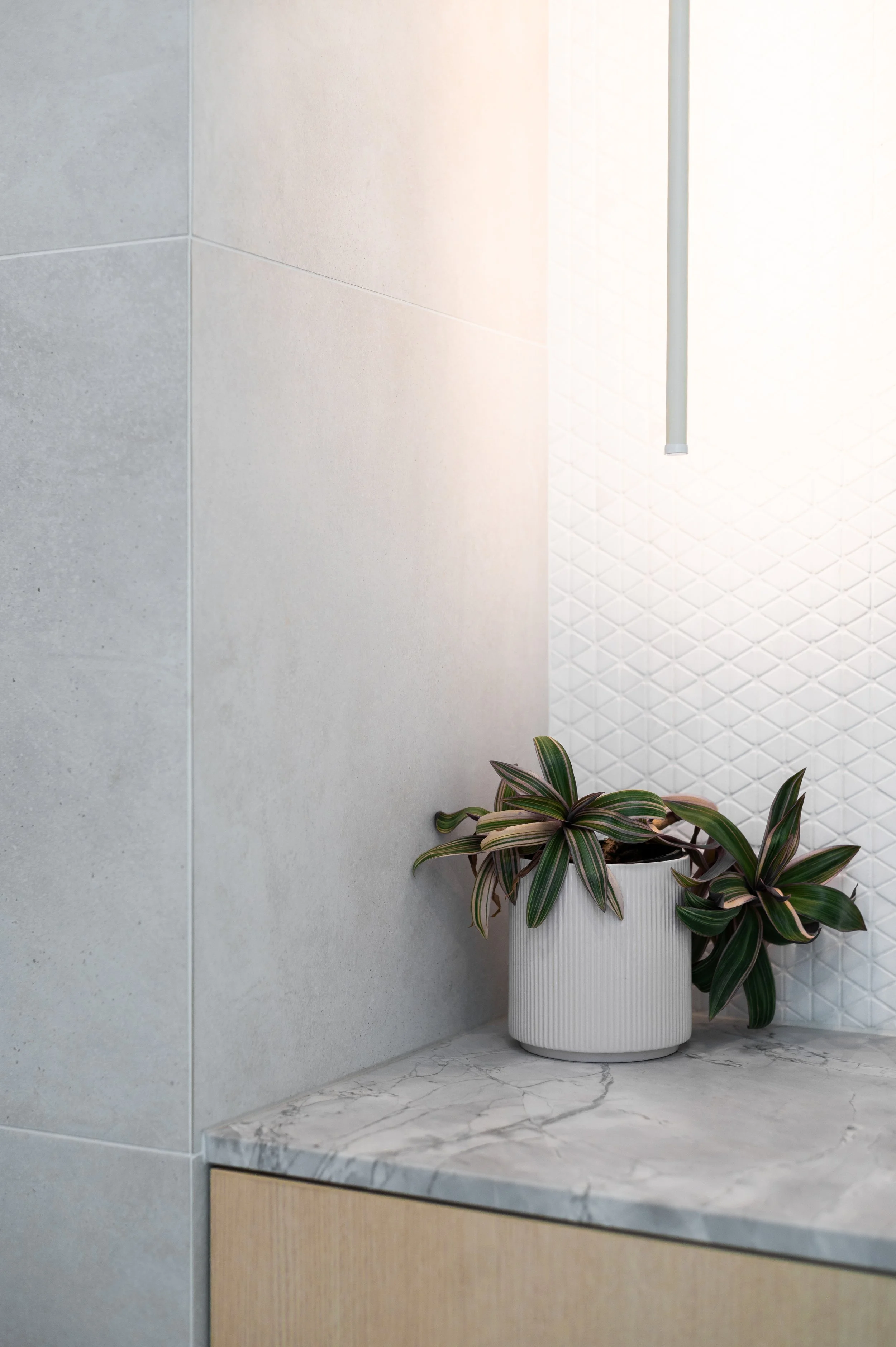 Brighton powder room detail showing stone benchtop, marble mosaic feature tiles, wood veneer vanity, and neutral grey tiles with integrated lighting