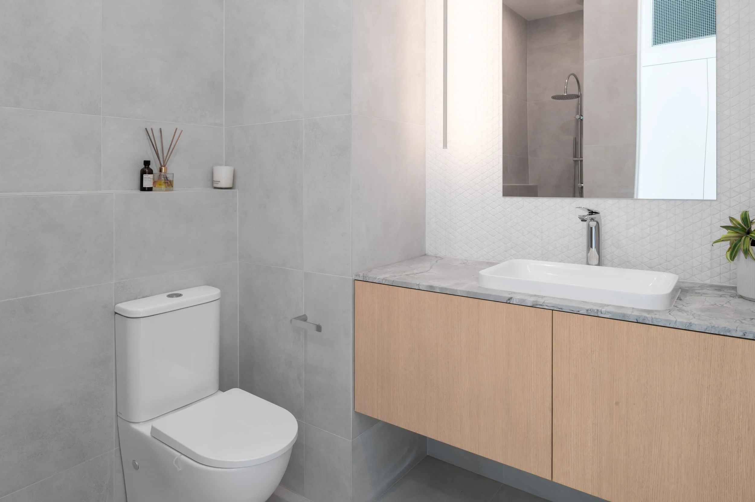 Brighton powder room showing the basin, toilet, and stone ledge, with marble mosaic feature tiles, wood veneer vanity, and neutral finishes for a contemporary, clean aesthetic