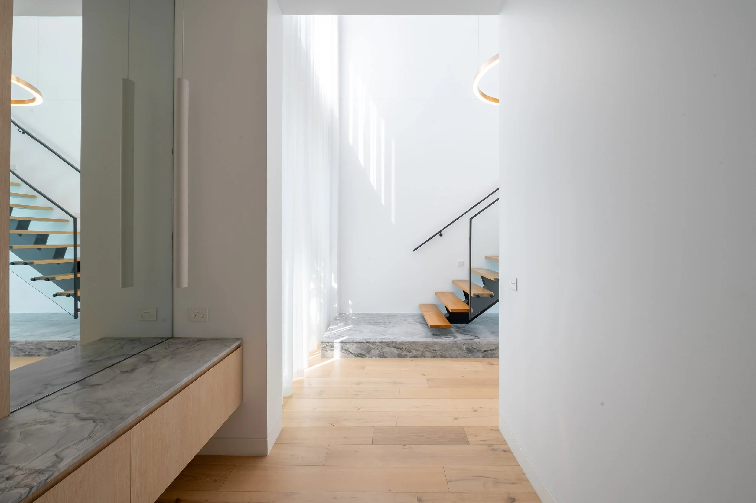 View of the Brighton entry featuring a built-in bench with ceiling-to-floor mirrors, decorative lighting, and staircase landing clad in Dolomite Super White natural stone