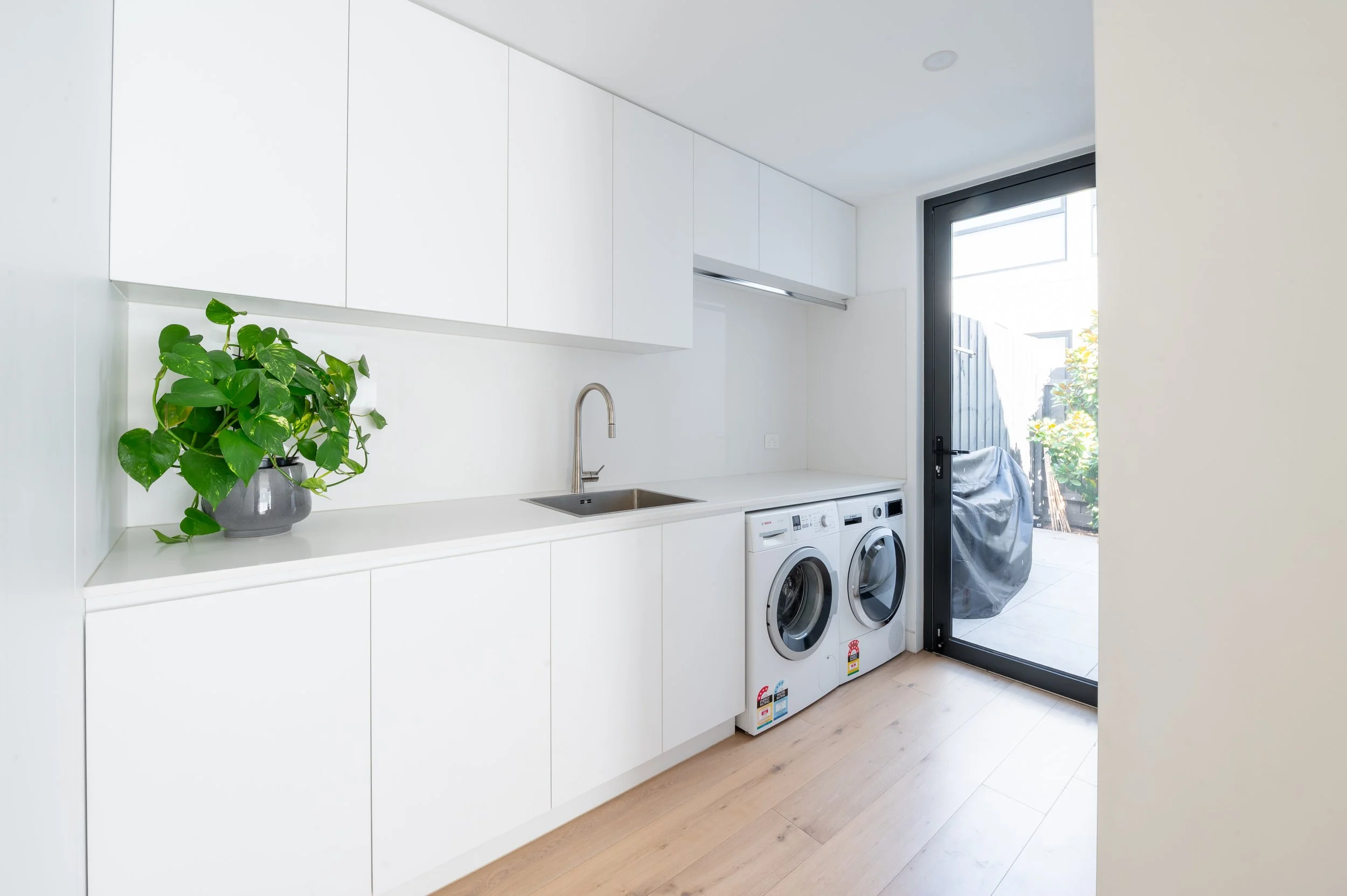 Brighton laundry situated behind the kitchen, with access to the garage on one side and the outdoors on the other, featuring clean, functional joinery and finishes.
