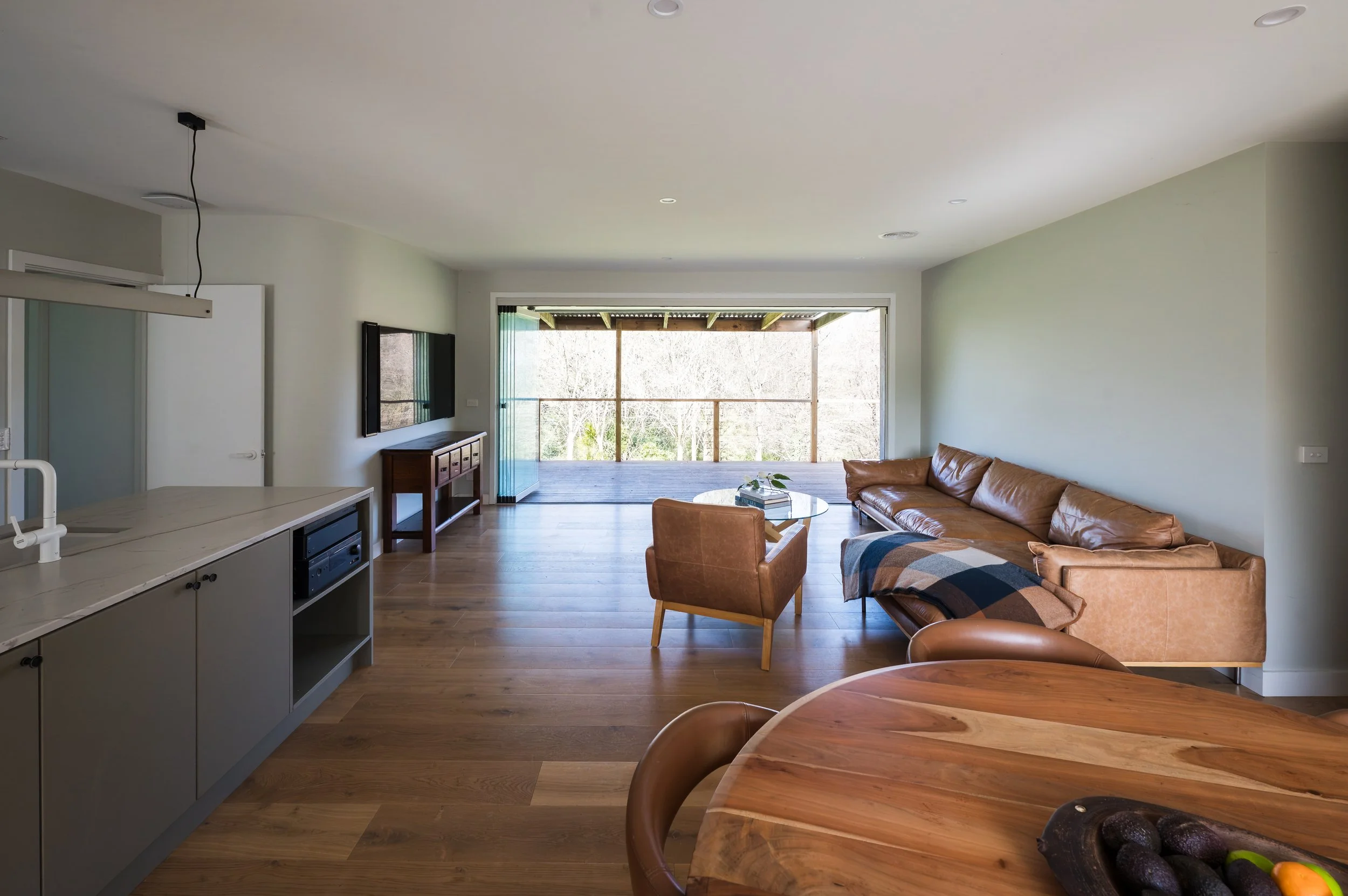 View from the entry of the Country Victoria home showing the kitchen to the left, dining to the right, and living area opening through full-height glass stacker doors to the verandah and valley views.