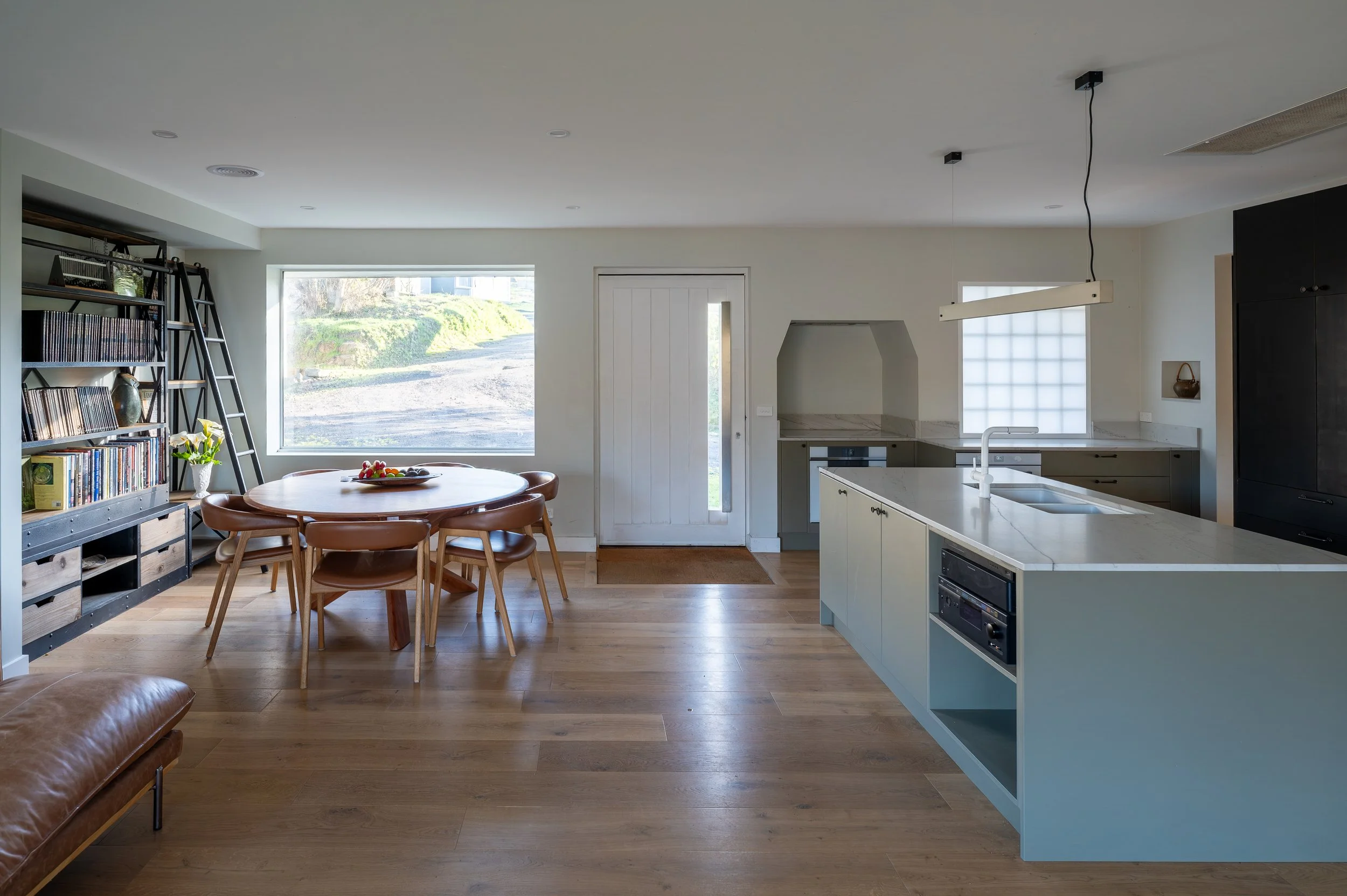 View from the lounge of the Country Victoria home, showing the open connection to the kitchen, dining, and entry areas, with natural light flowing through full-height glass stacker doors.