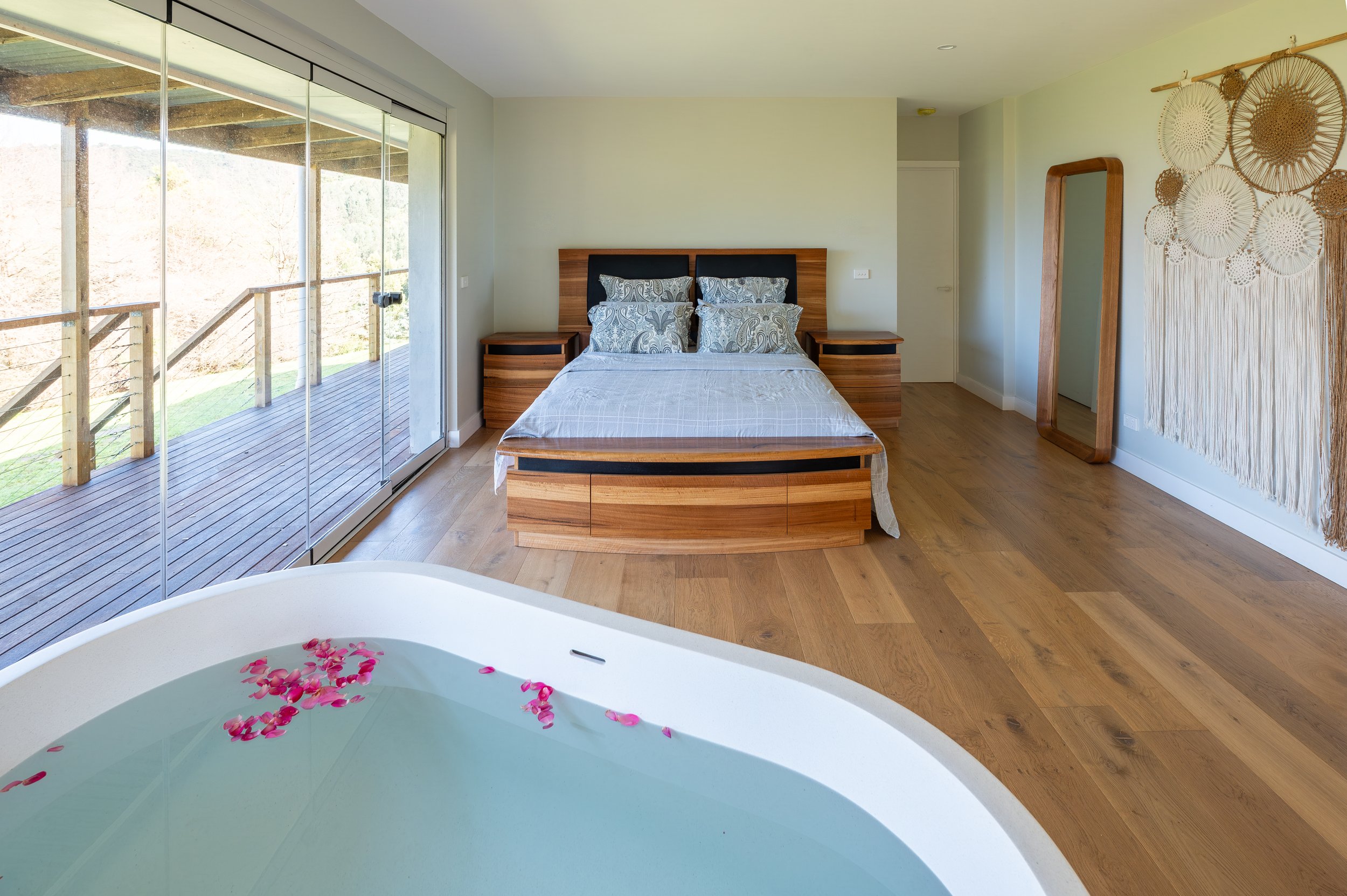 View from the bathtub in the master bedroom of the Country Victoria home, looking towards the bed and full-height stacker doors opening to valley and distant sea views.