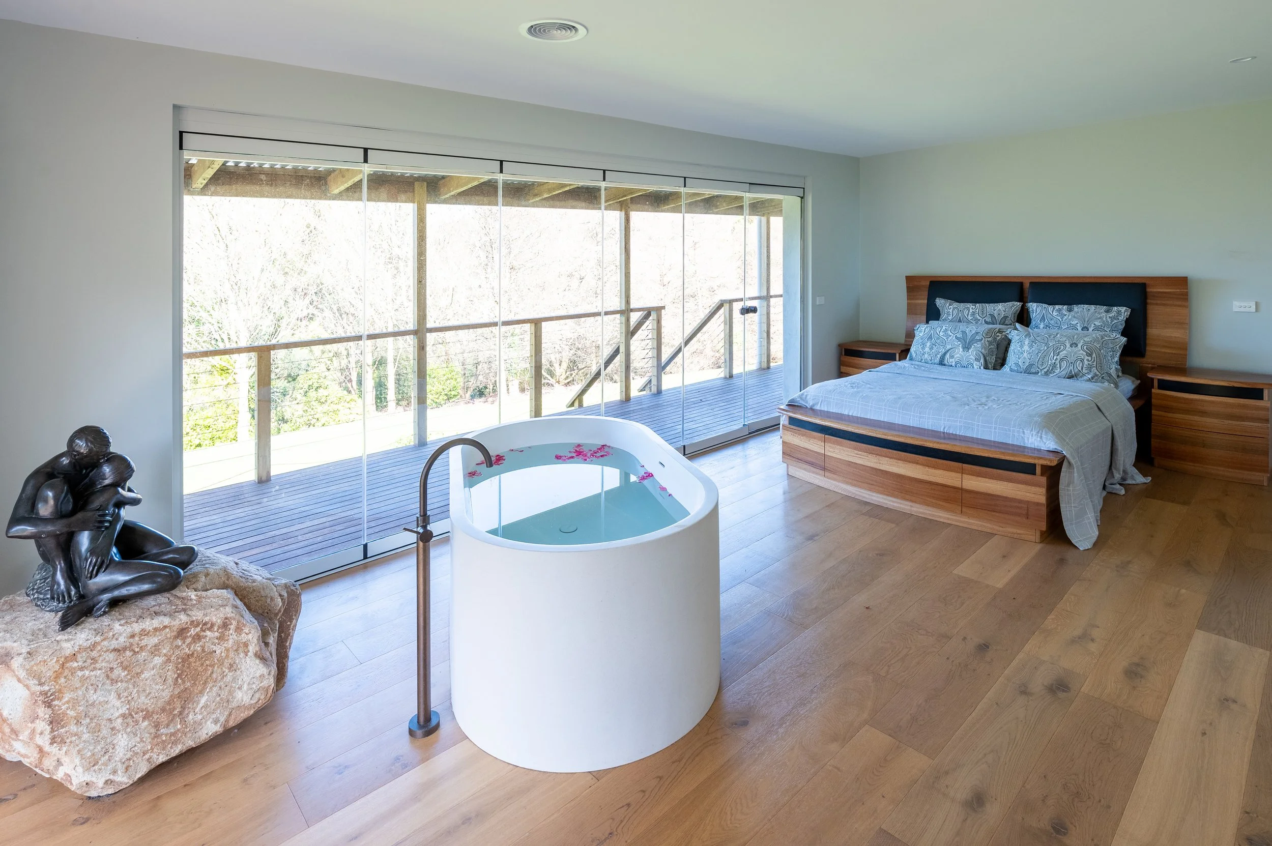 Main bedroom with floor to ceiling glass doors opening to valley and distant ocean views, filled with natural light and indoor outdoor flow