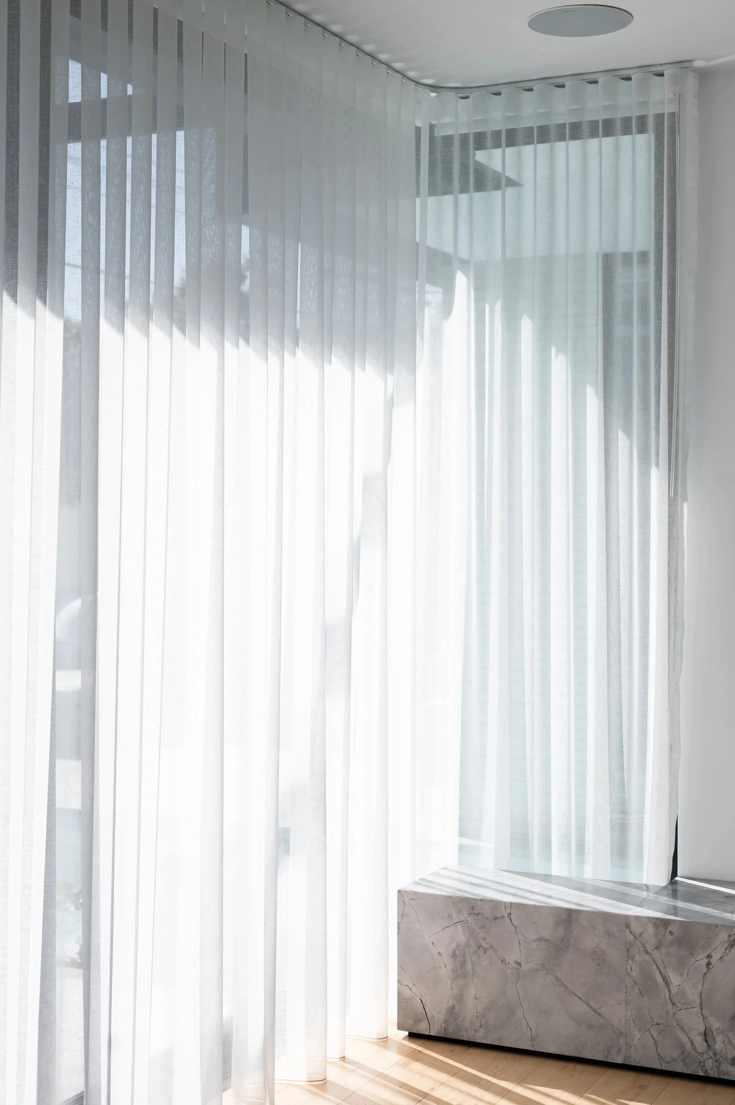 Close-up of the Brighton Project living room entertainment unit, showing integrated storage and the sheer curtain positioned behind the unit as part of the design.