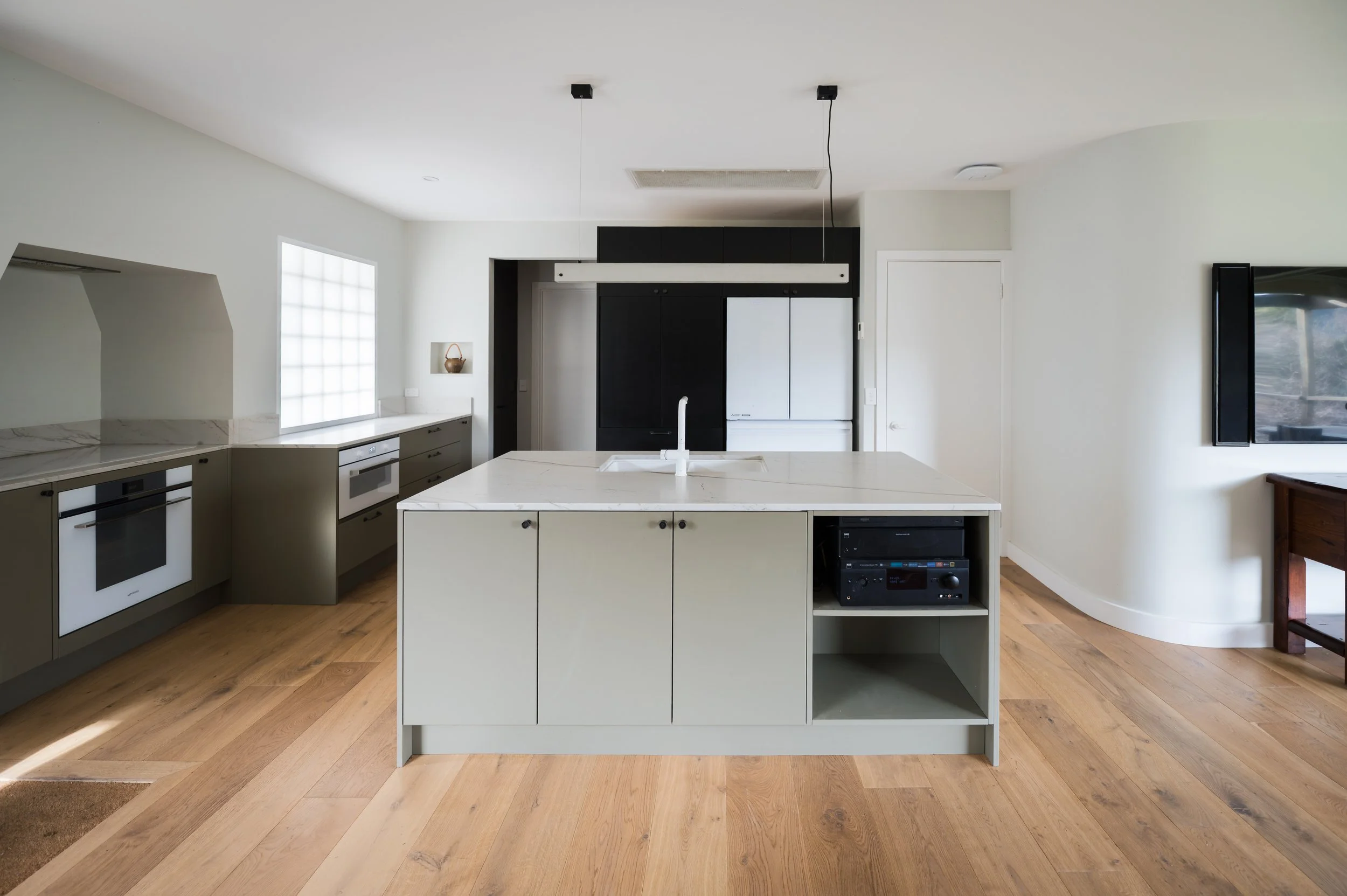 Country Victoria kitchen featuring custom black joinery for integrated appliances, Mont Blanc quartzite benchtops, light eucalyptus green cabinetry, Smeg appliances, diffused glass bricks, and a concrete pendant light by Bentu.