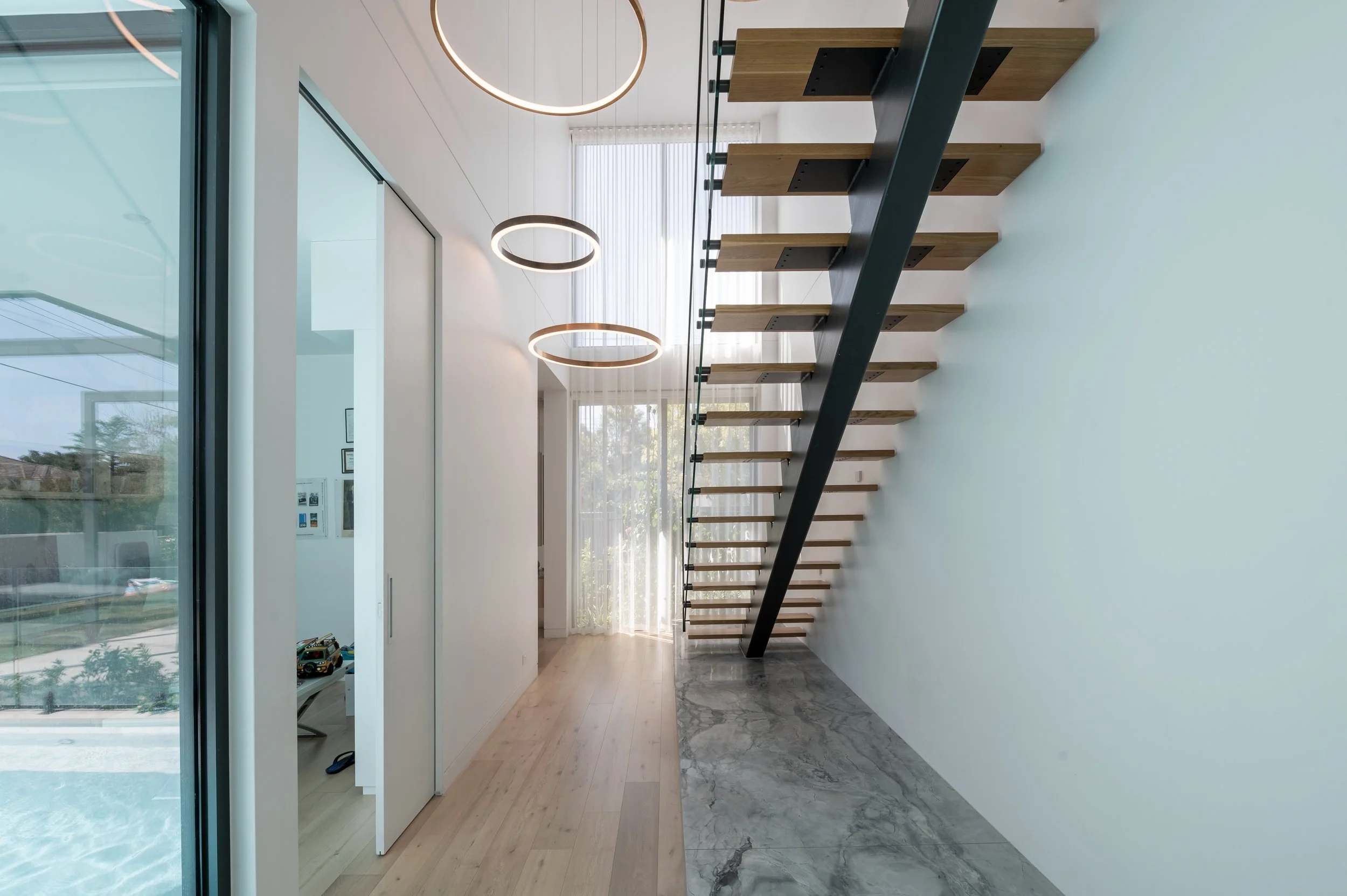 View from the Brighton staircase towards the entry, showing decorative lighting in the void, stone platform detail, study overlooking the pool, and the pool to the left.