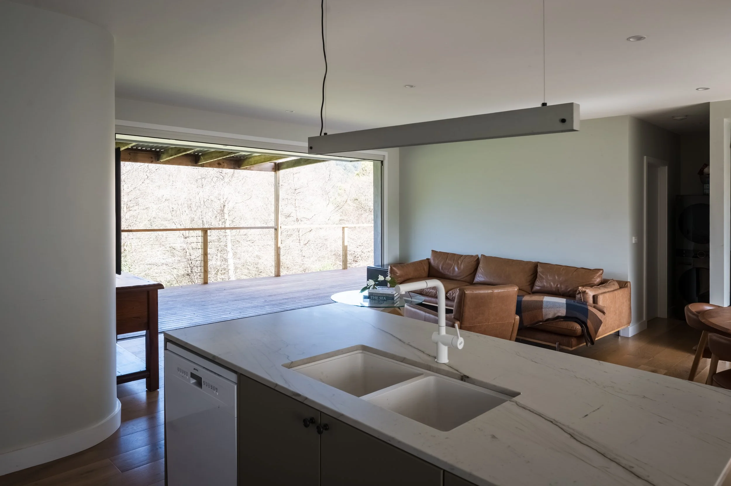 View from the kitchen sink looking out through full-height, wall-to-wall glass stacker doors to the valley landscape at the Country Victoria residence.