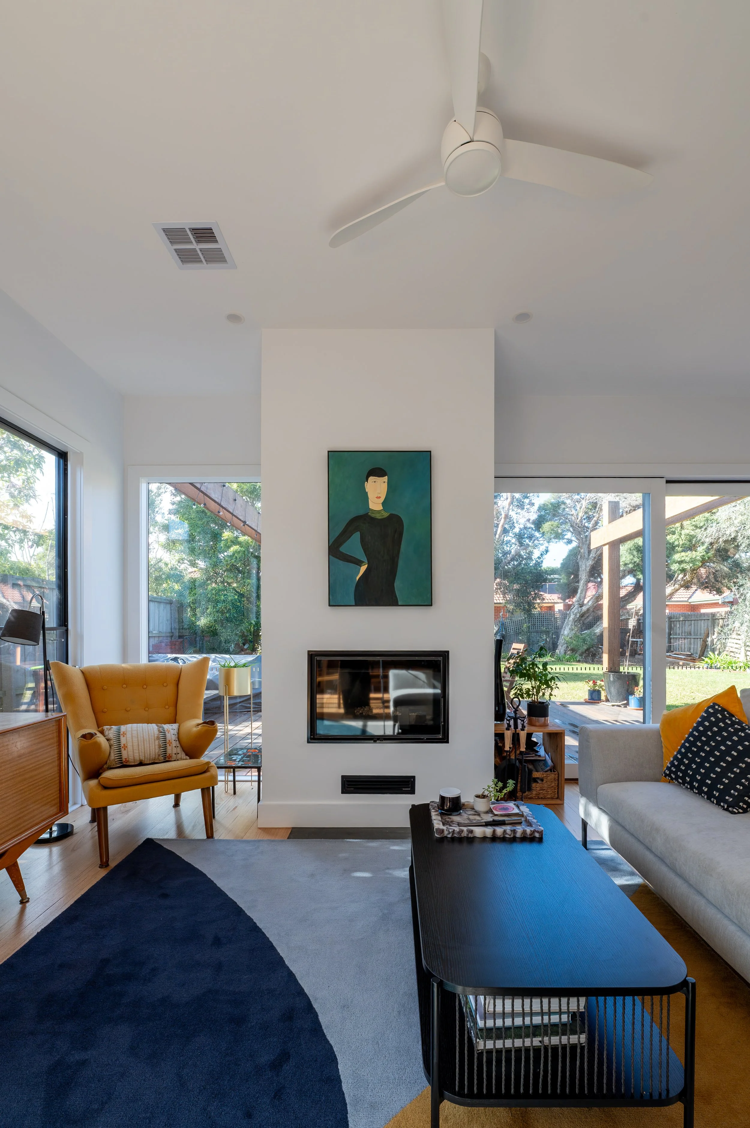 Oak Street residence open-plan living and dining area redesigned to incorporate the owners’ existing furniture, featuring a fireplace, seamless flow to the rear deck, and cohesive joinery and finishes.