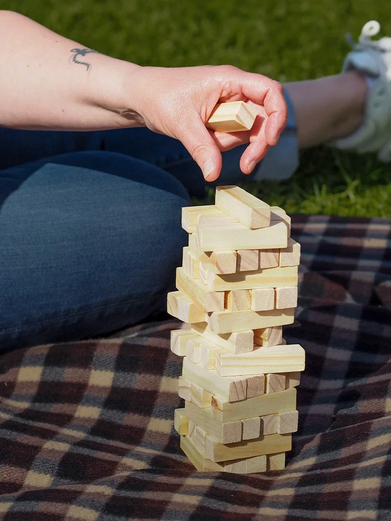 Kuva vihreällä nurmikolla istuvasta ihmisestä, joka asettelee puisia palikoita päällekkäin torniksi.