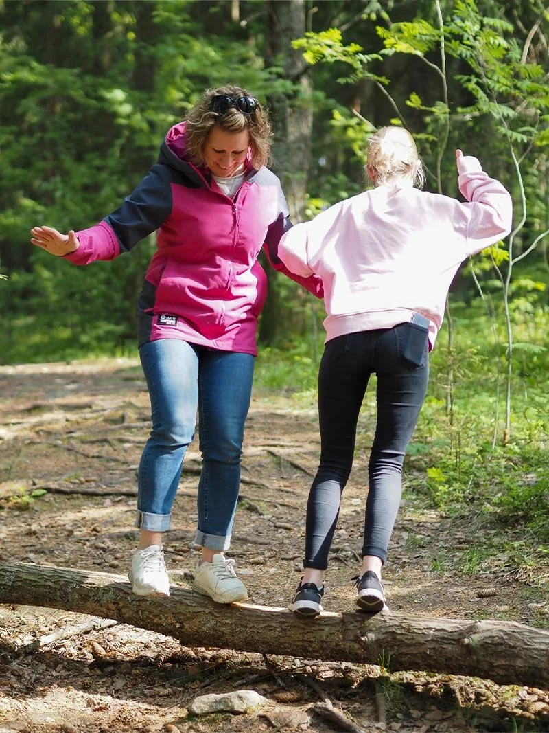 Nepsy-valmentaja ja asiakas tasapainoilevat metsässä puunrungon päällä.