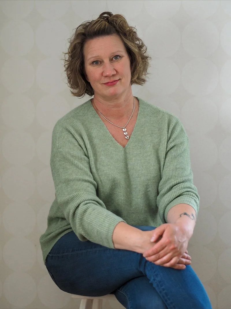 Työnohjaaja Mia Pyykkö istuu jakkaralla kädet polvien päällä, asuna vihreä neule ja siniset farkut.