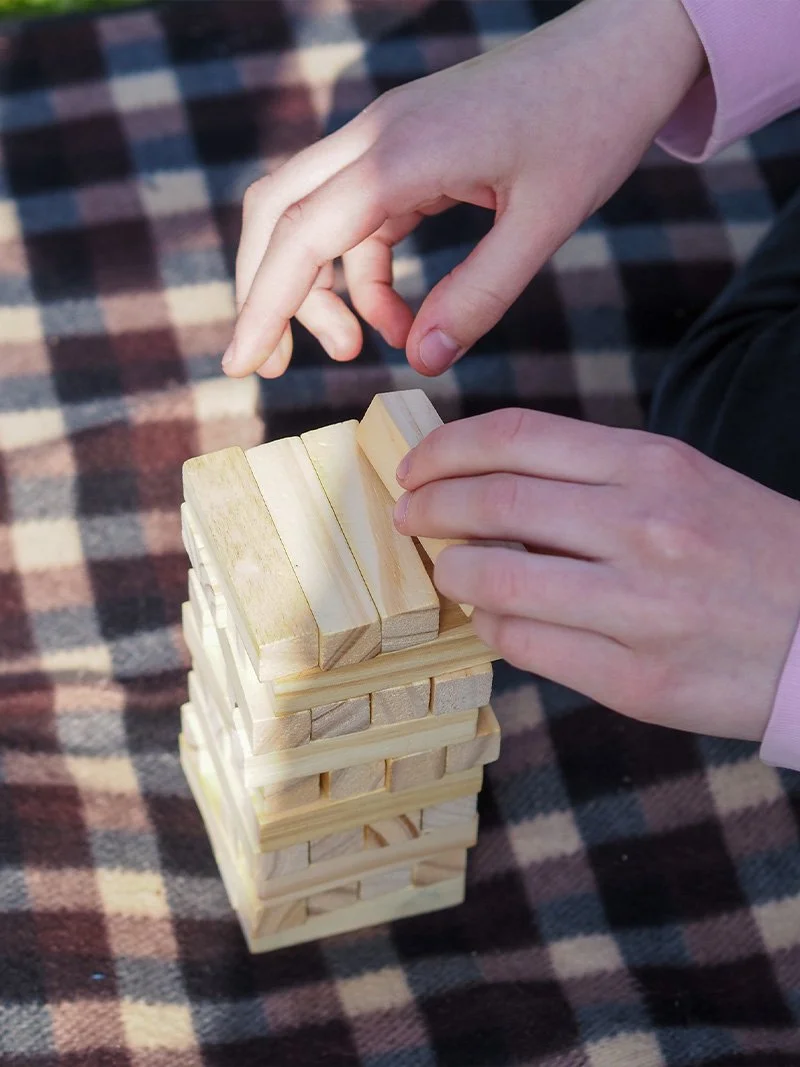Sormet rakentavat tornia puisista paloista, jotka on aseteltu päällekkäin ruudullisen viltin päälle.