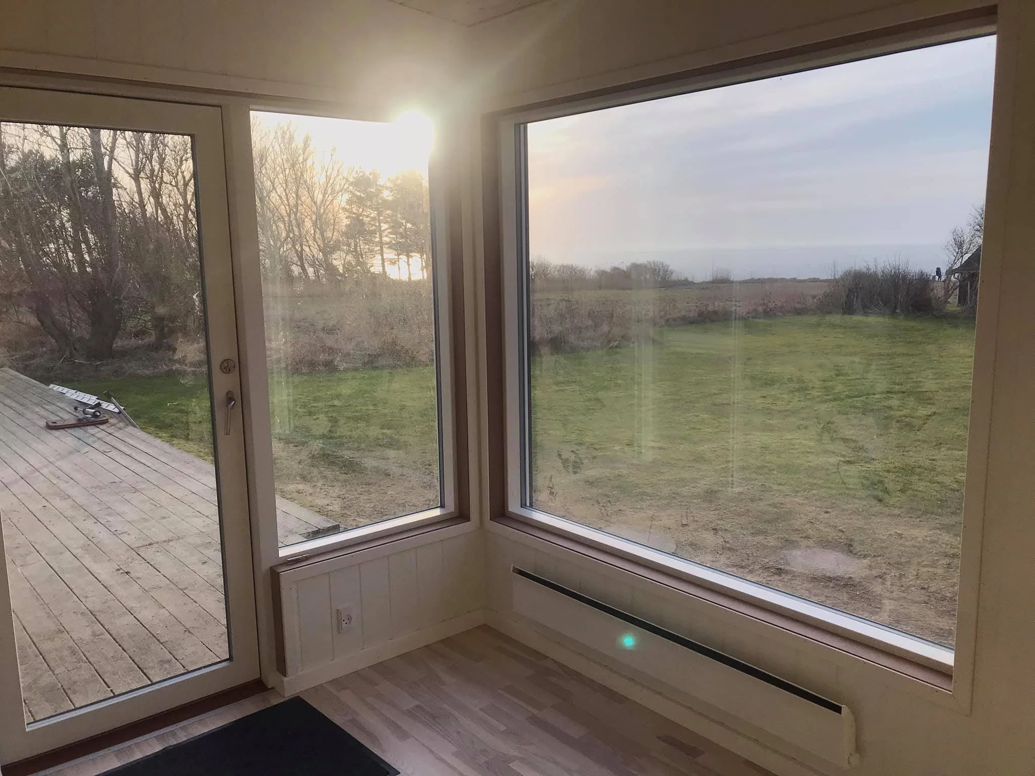 Indendørsvindue med udsigt til udendørs græsareal og træer i solnedgang.