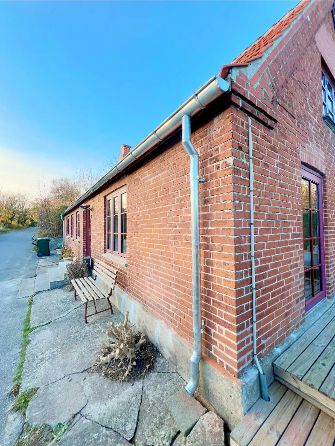 Udendørs billede af et rødt murstenshus med vinduer, pap-løbere og nedløbsrør, under en blå himmel.