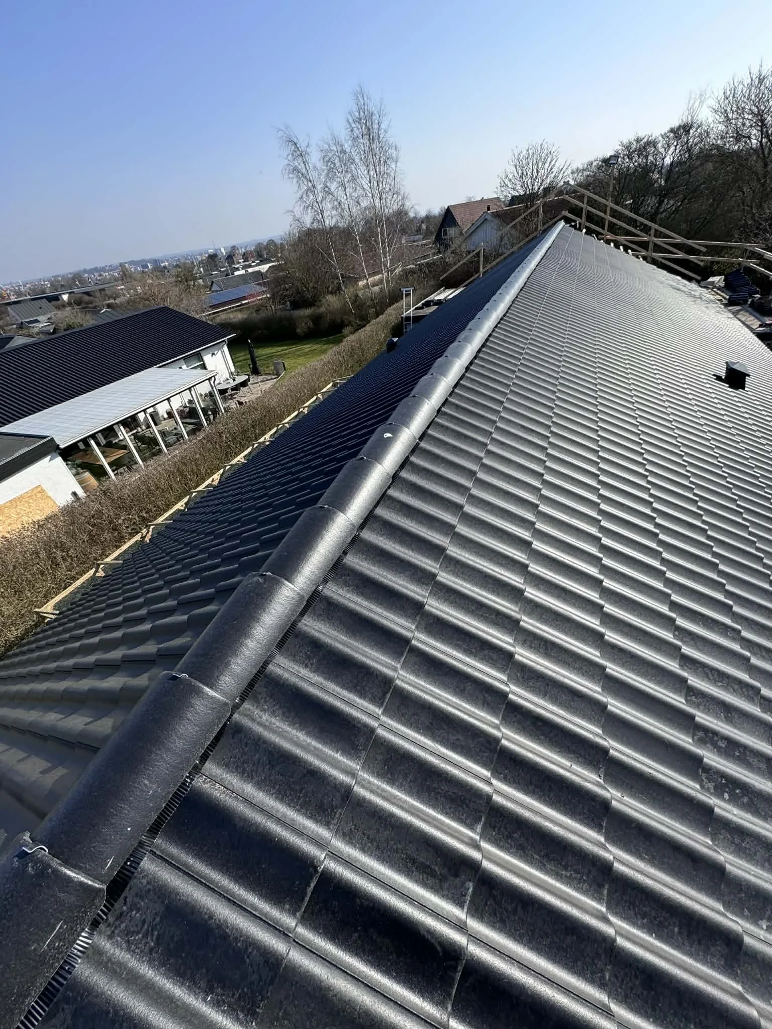 Billedet viser en tagflade med nyudskiftede tagbølgeblade i blå grå farve på et hus, set fra oven.