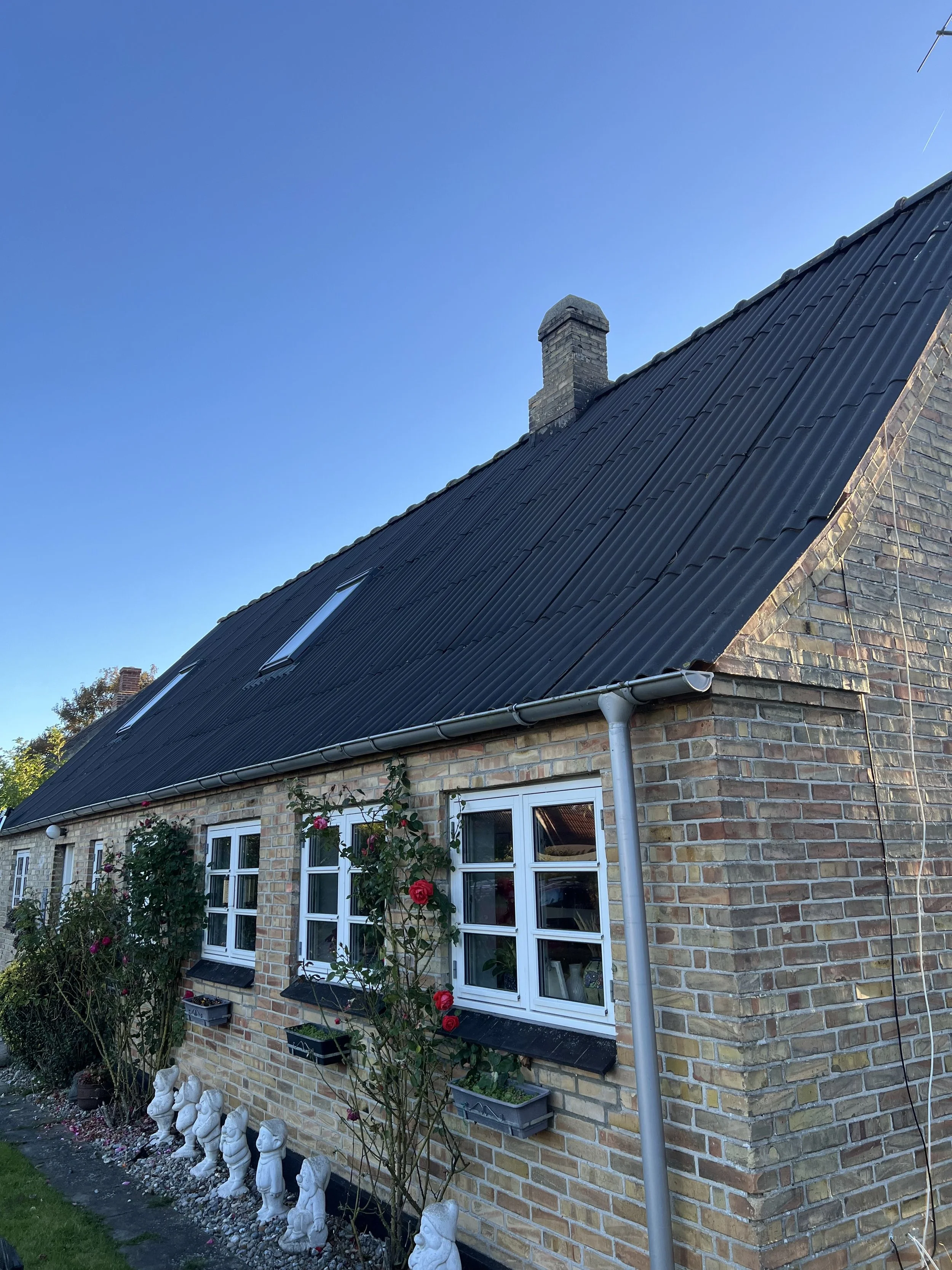 En stenhus med sort tag, hvide vinduer og blomster foran