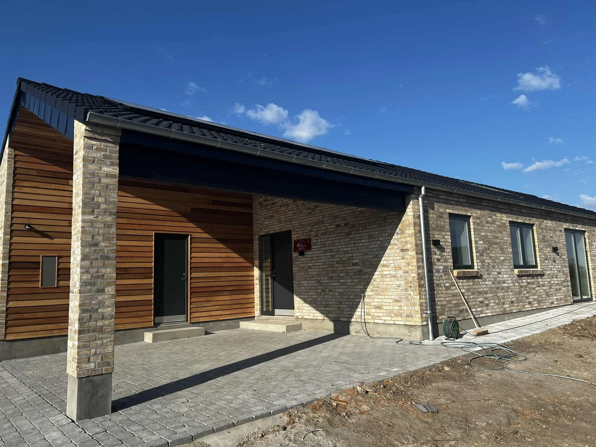 Nyt byggeri med kombination af mursten og træfacade under opførelse, med udendørs areal, og klar til brug.