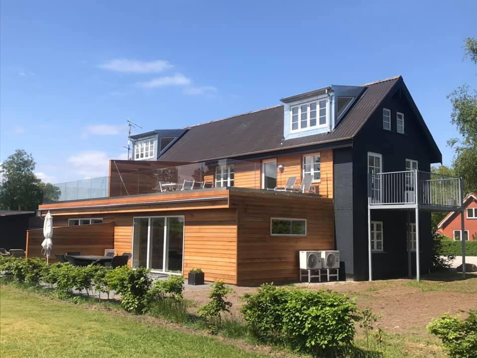 Et moderne hus med træfacade, store vinduer, balkon og tagterrasse med havemøbler.