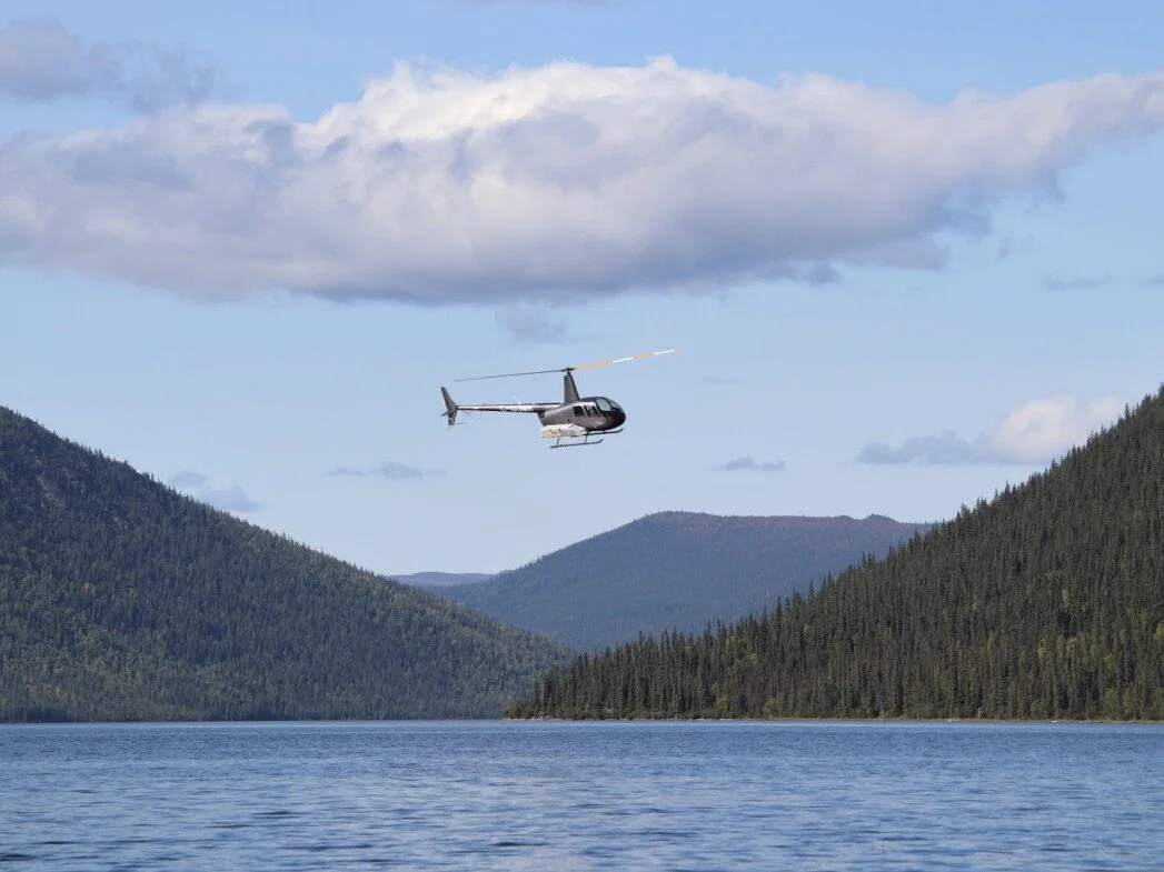 Un hélicoptère volant au-dessus d'un lac entouré de montagnes boisées par une journée ensoleillée avec des nuages.