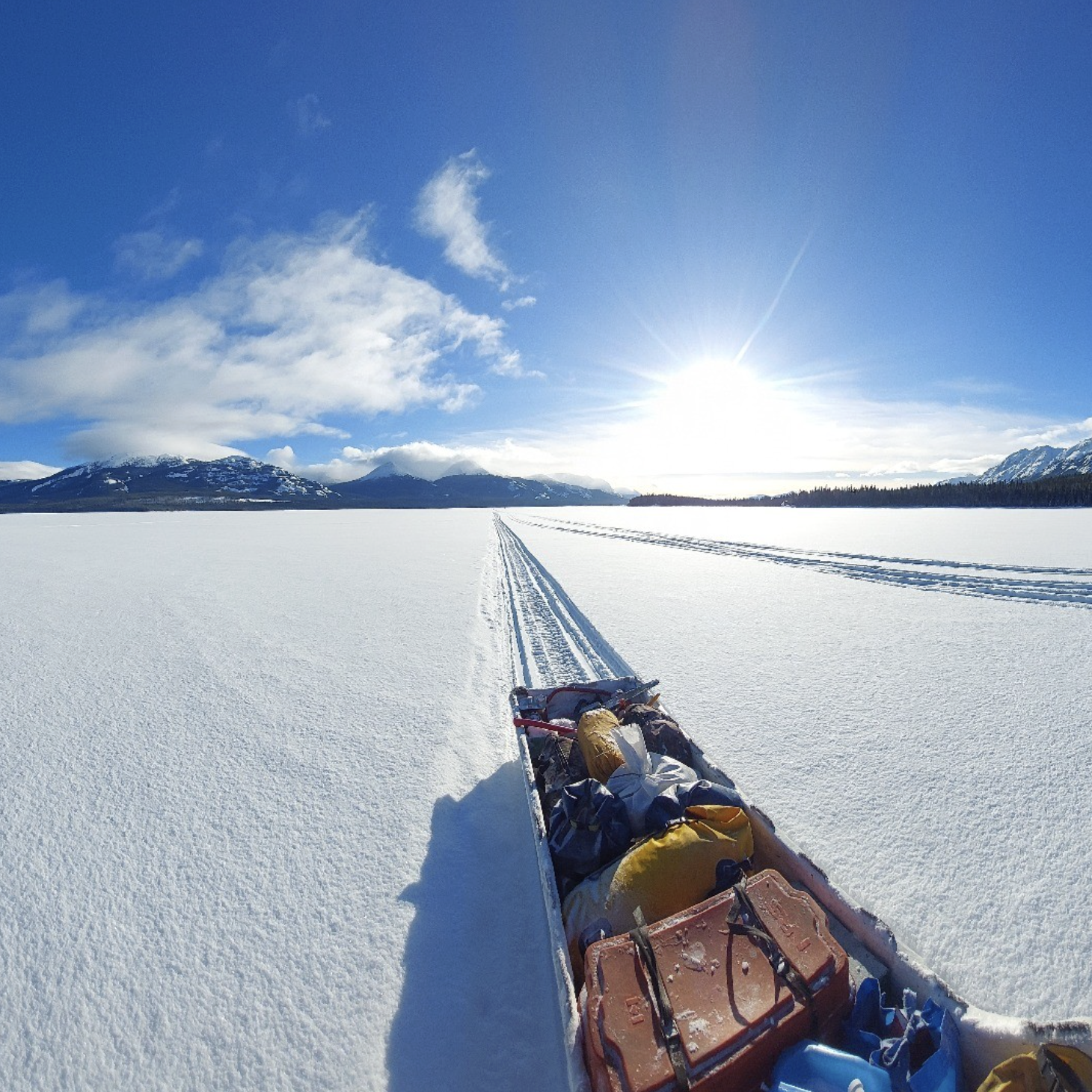 Traîneau à neige avec équipement dans un paysage de neige en montagne, ciel bleu, soleil brillant.