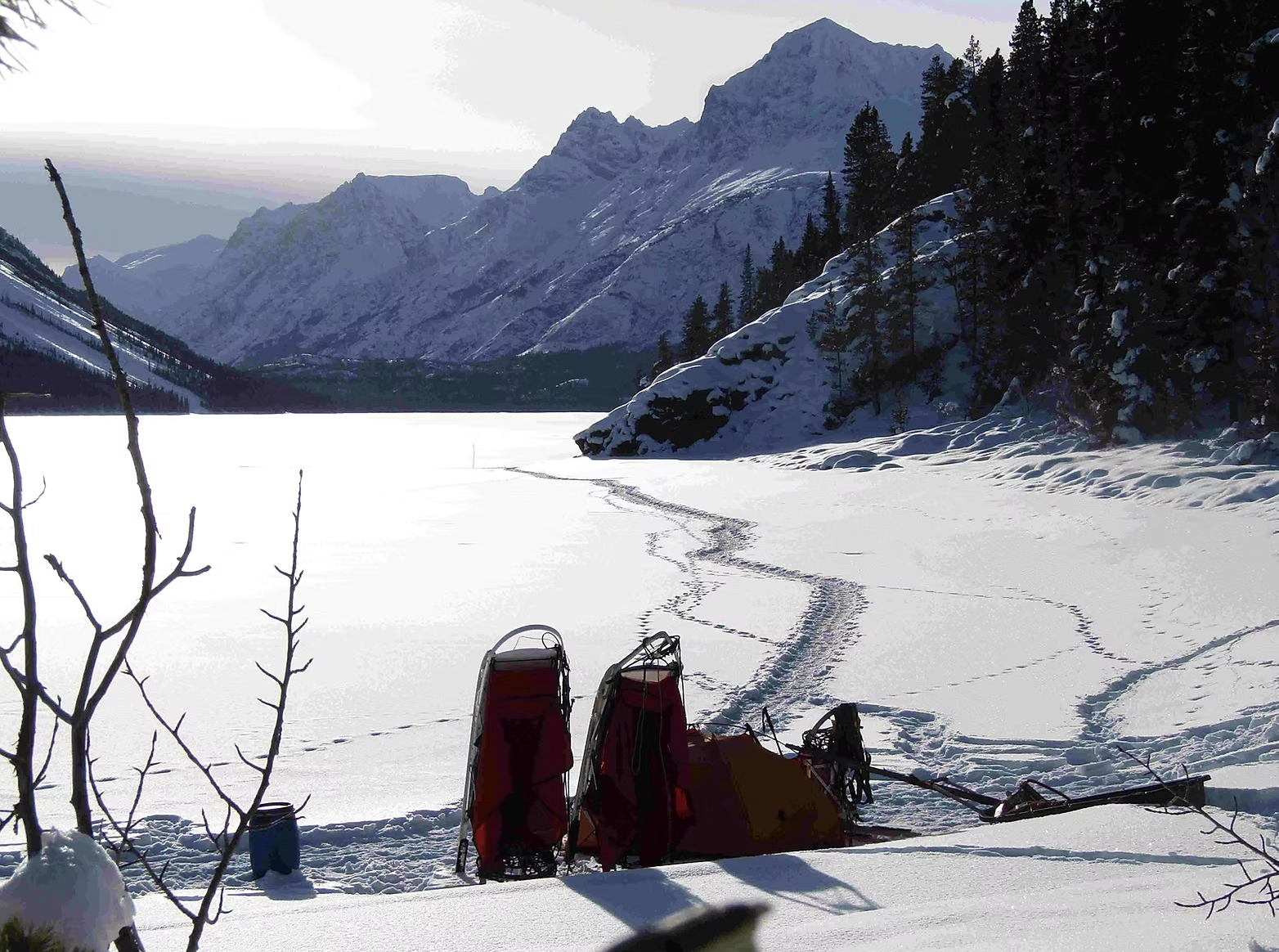Trousses de secours et skis dans un paysage enneigé avec montagnes et arbres, près d'un lac gelé.