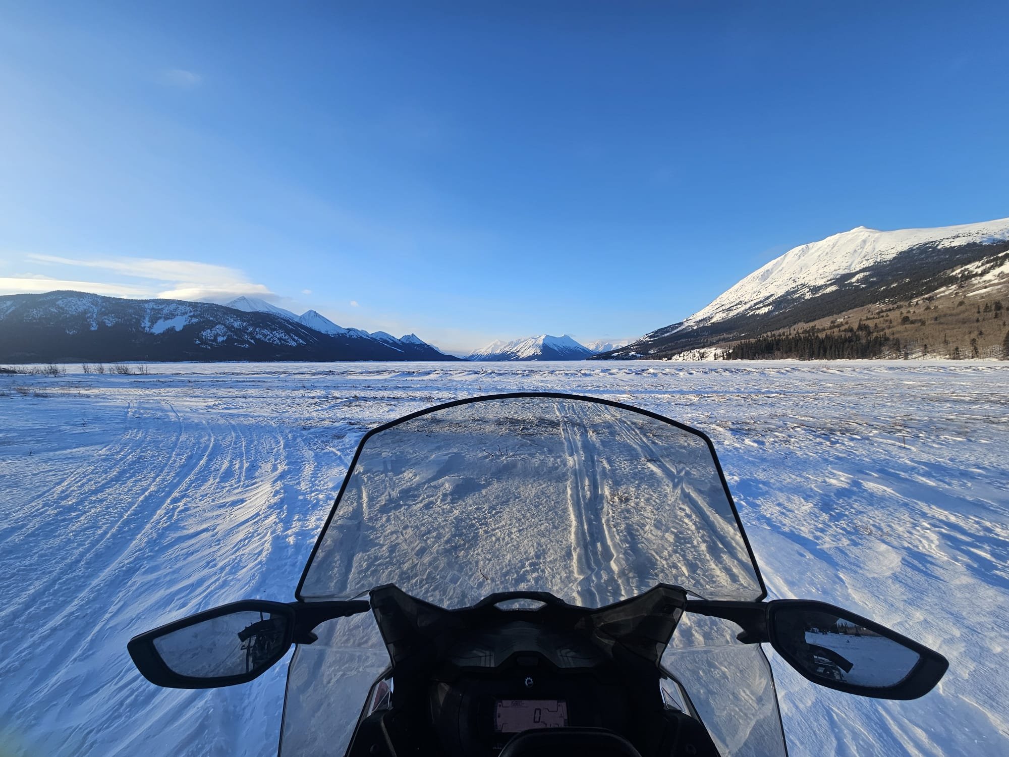 Vue depuis un scooter des neige sur un paysage de montagnes enneigées sous un ciel bleu.