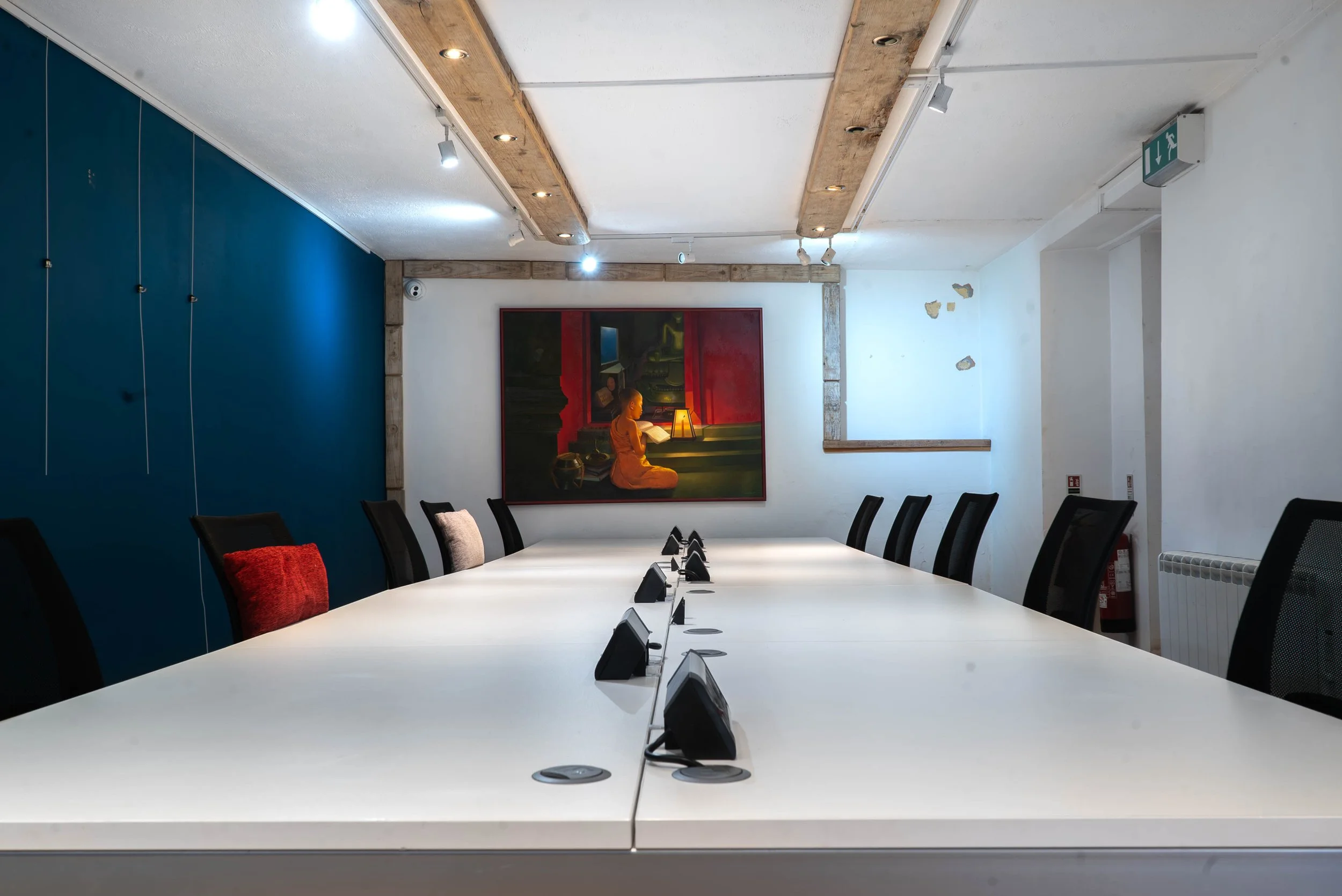 Empty conference room with a long white table, black chairs, and a colorful mural painting on the wall, with some wear marks on the wall.