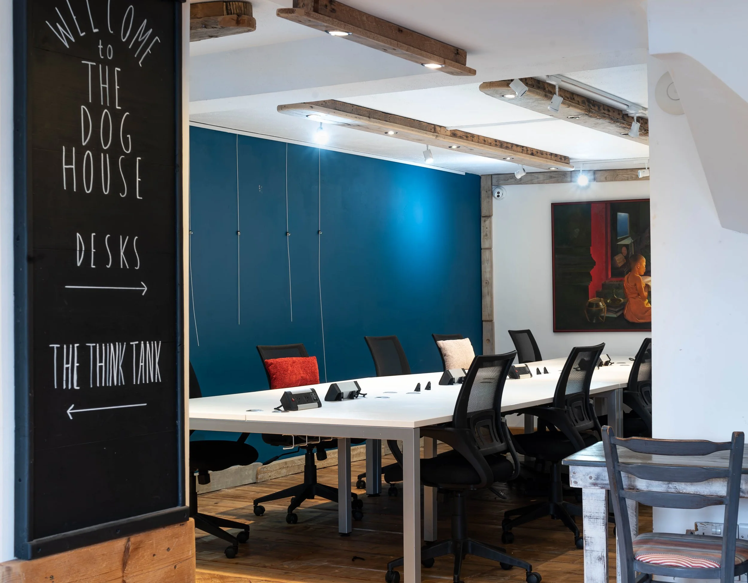 Conference room with white table, black chairs, and a blue accent wall, with art and a welcome sign in the foreground.