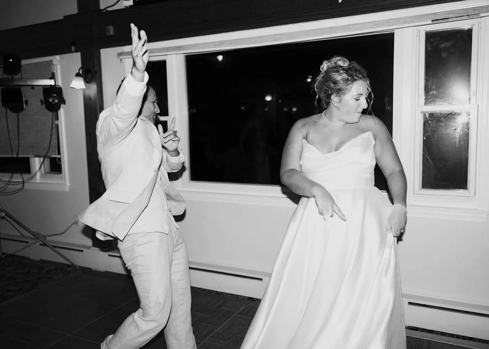 Bride and groom dancing playfully during a lively wedding reception at a coastal venue, captured with candid flash photography.