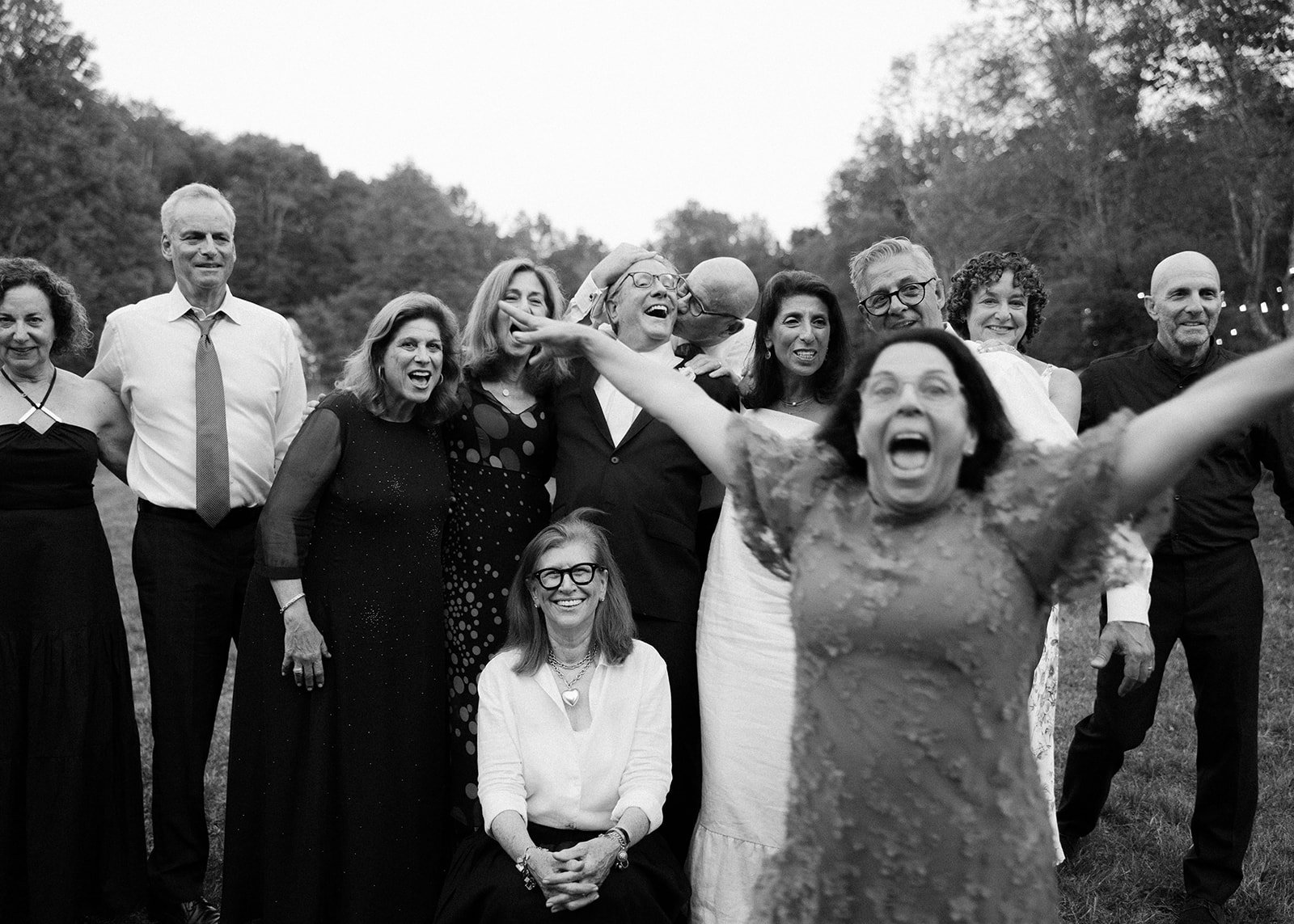Joyful family group portrait with a woman jumping in the foreground, capturing fun and candid wedding energy.