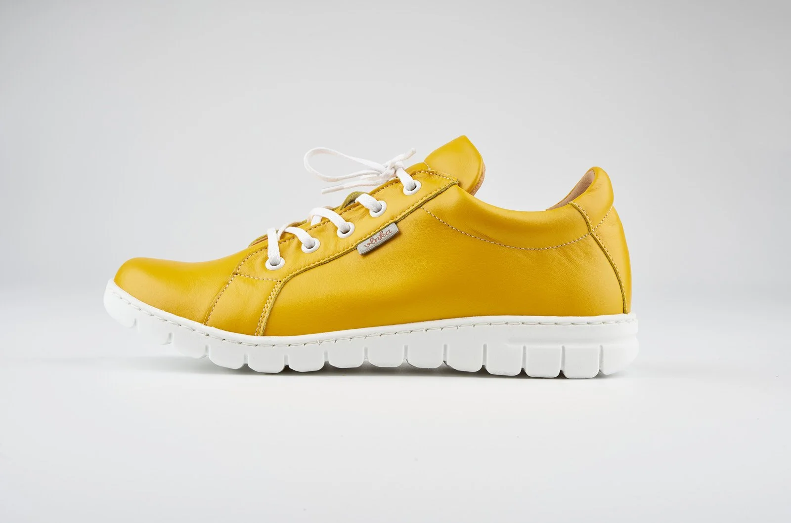 Yellow leather sneaker with white sole and laces on a plain white background.