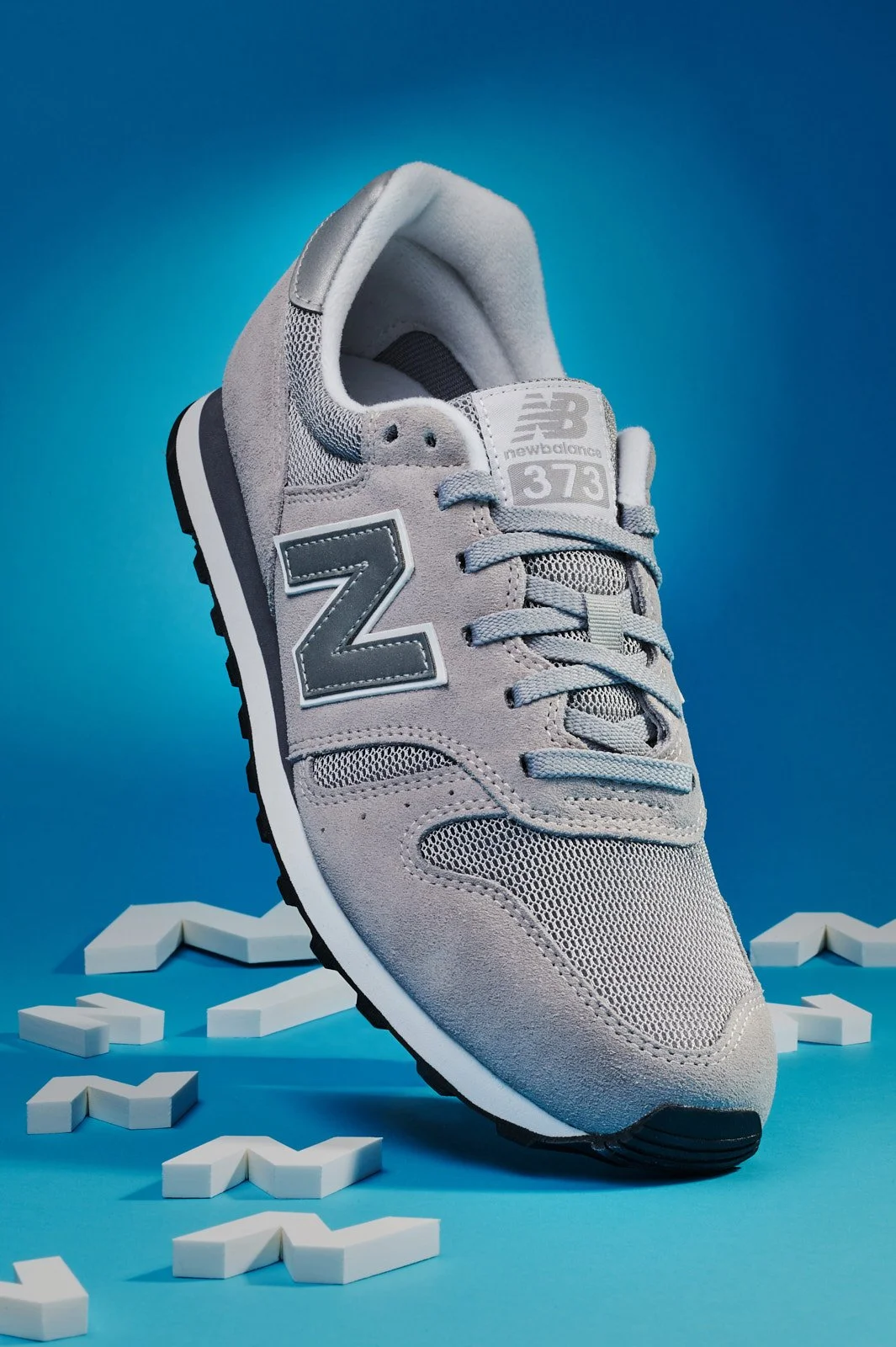 Gray New Balance sneaker shoe on a blue background with white puzzle piece shapes around it.
