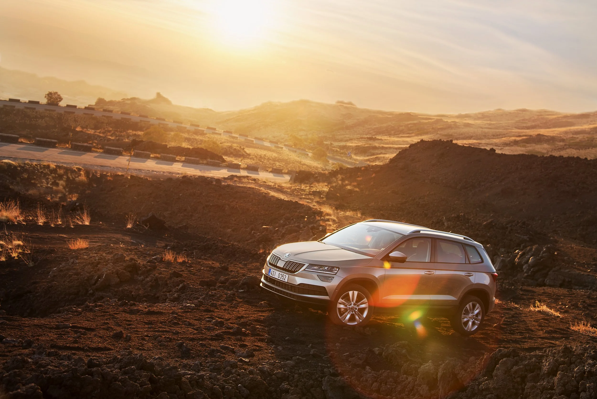 A modern SUV driving on a rugged terrain with a sunset in the background and rolling hills in the distance.
