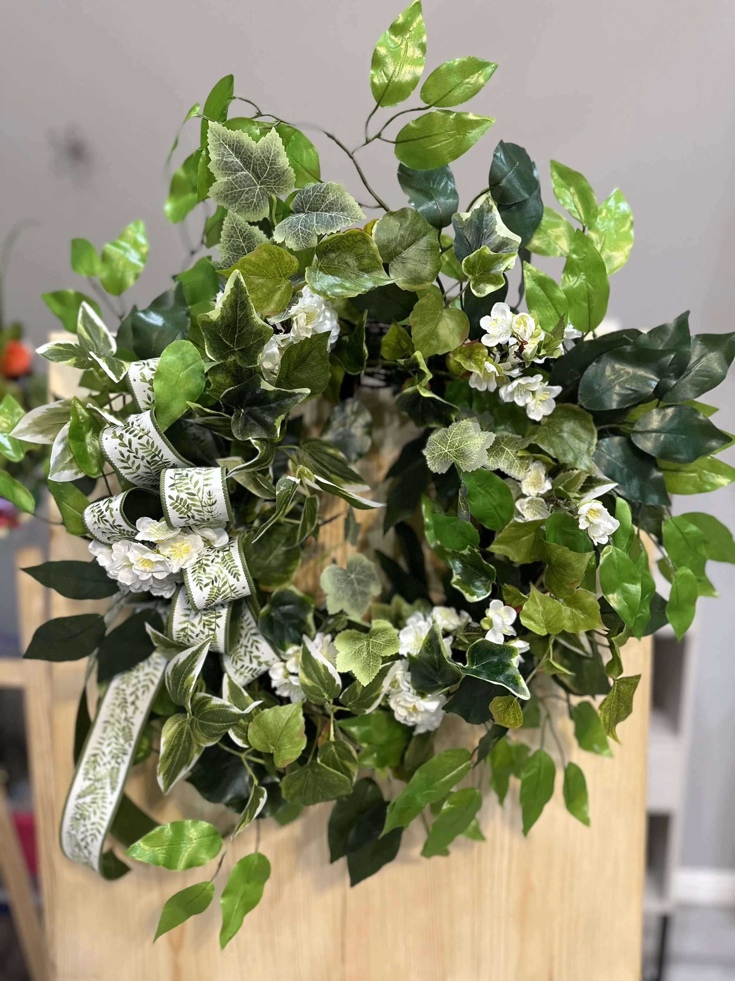 Plant arrangement with green and variegated leaves, white flowers, a decorative ribbon, on a wooden surface.