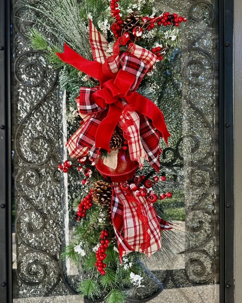 Decorative Christmas wreath with red ribbons, plaid bows, pinecones, red berries, and greenery, hanging on a window with metal scrollwork.