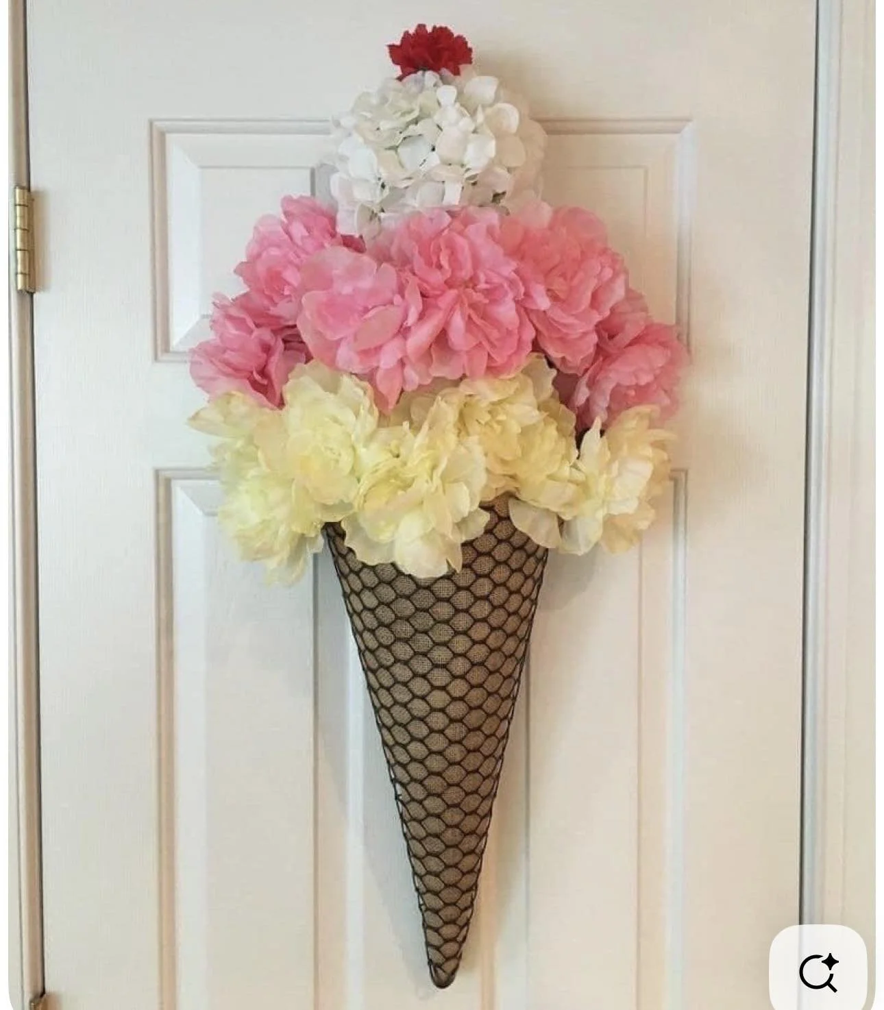 Decorative wall arrangement of artificial flowers resembling an ice cream cone with pink, yellow, white, and red flowers.