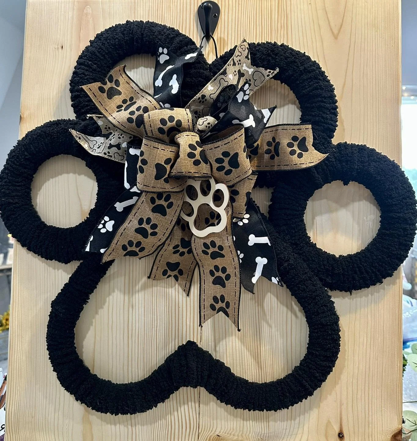Decorative wreath with black, brown, and white ribbon bows and a paw print ornament on a wooden background.