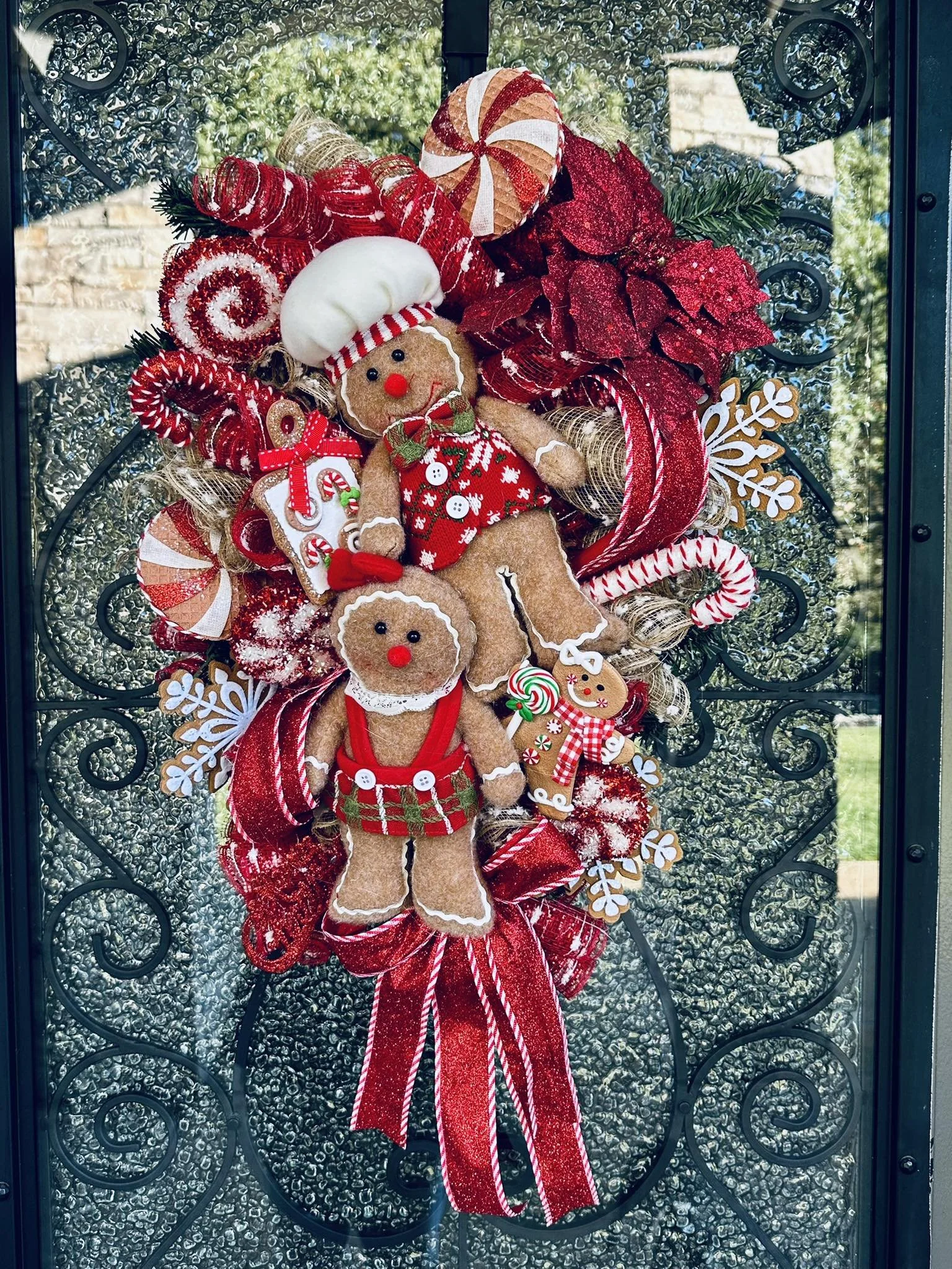 Red and white Christmas wreath on front door with gingerbread puppet decorations, candy canes, poinsettias, and holiday ribbons.