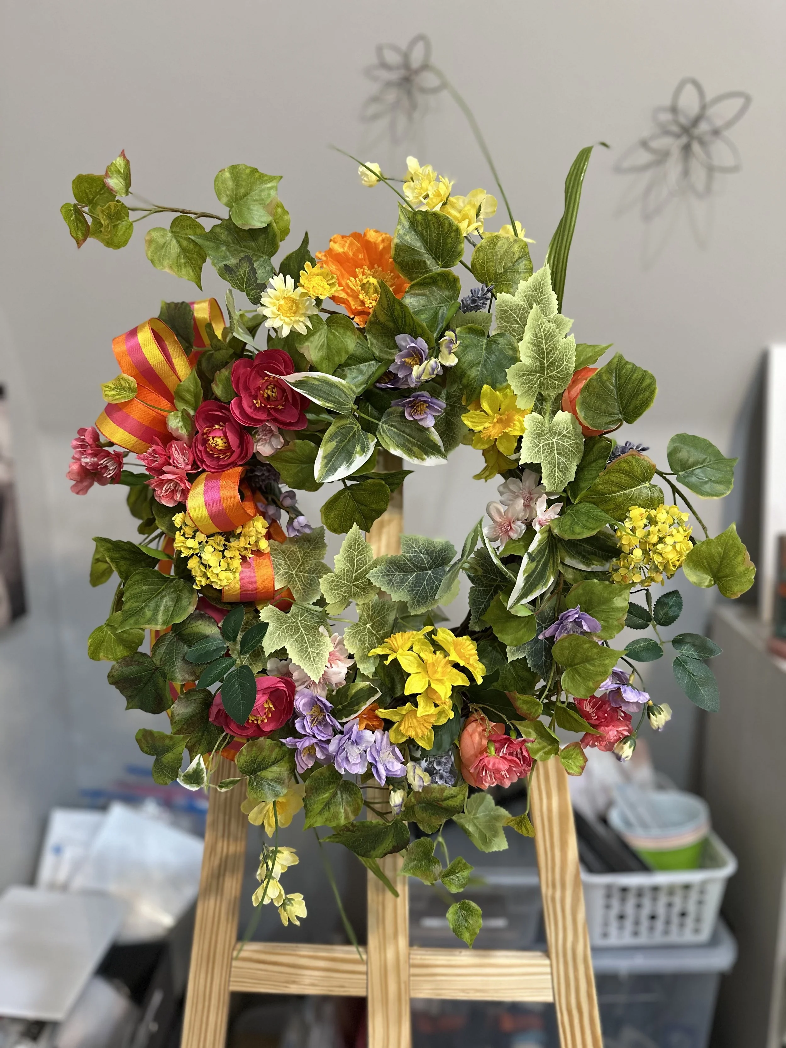 Colorful flower arrangement with mixed flowers, green leaves, and a ribbon, placed on a wooden stand.