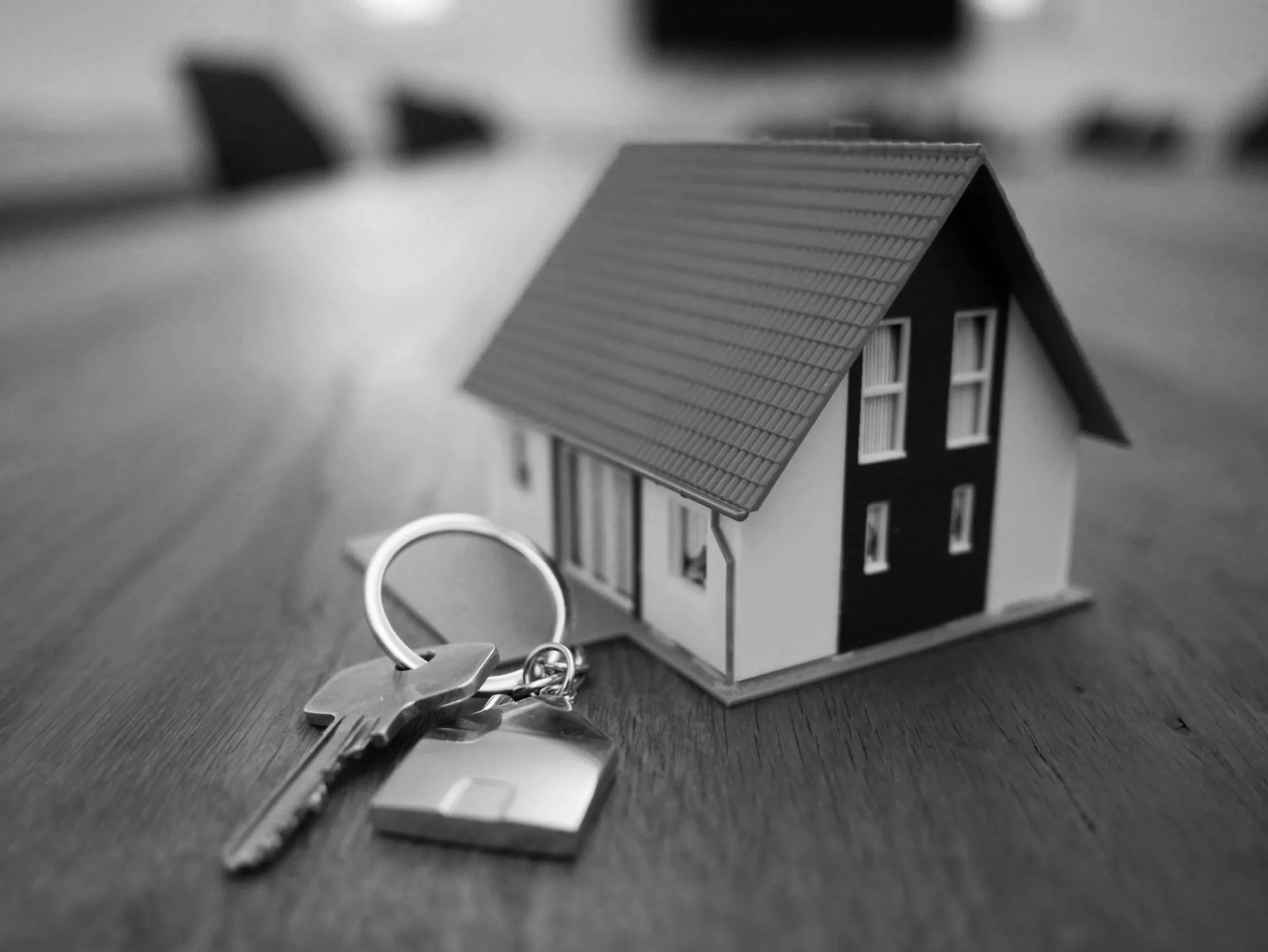 Llavero con llave en forma de casa y una maqueta de una casa de tamaño pequeño, todo en blanco y negro.