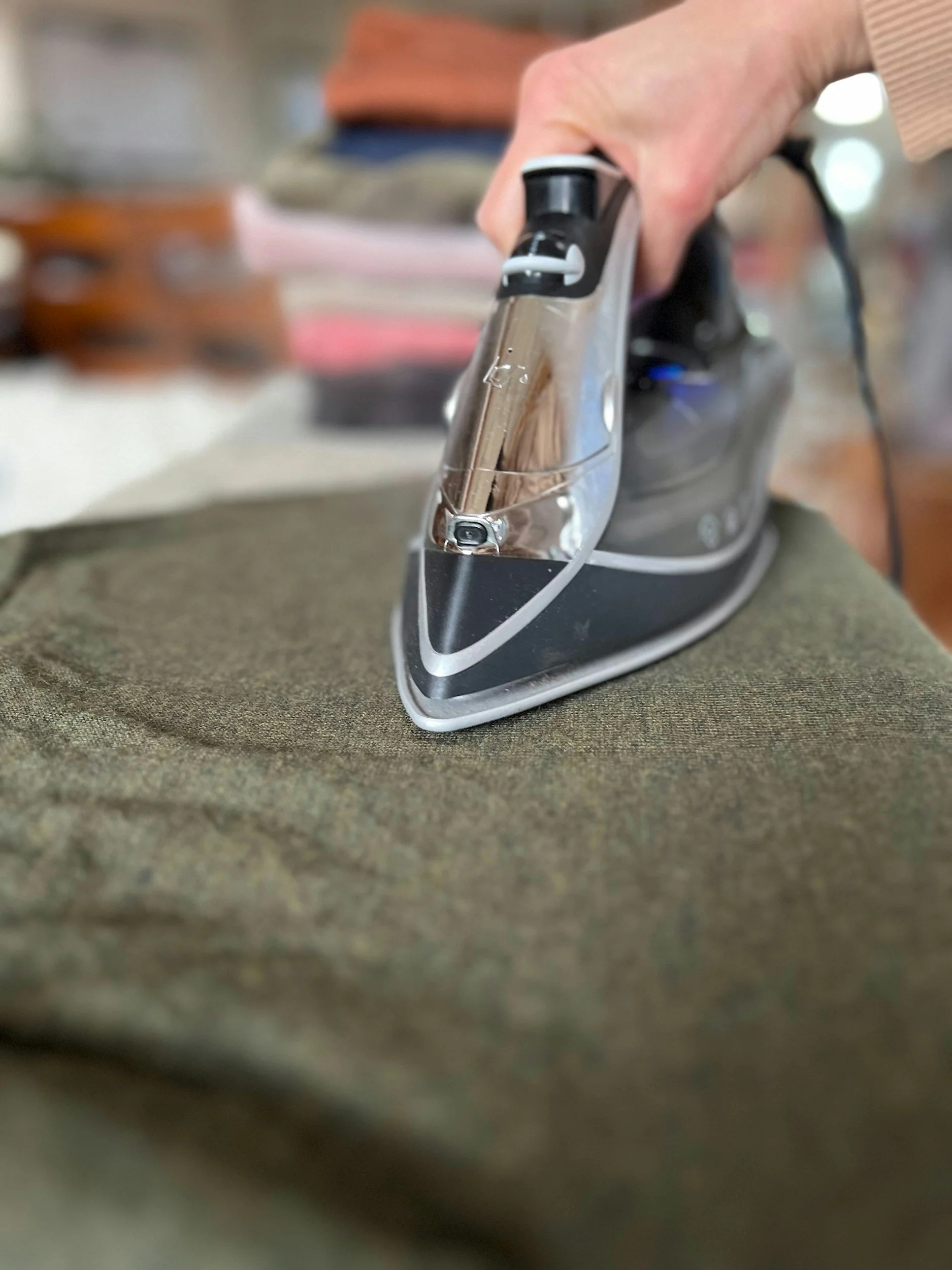 A person using a black and silver iron to press a piece of fabric, viewed from a low angle.