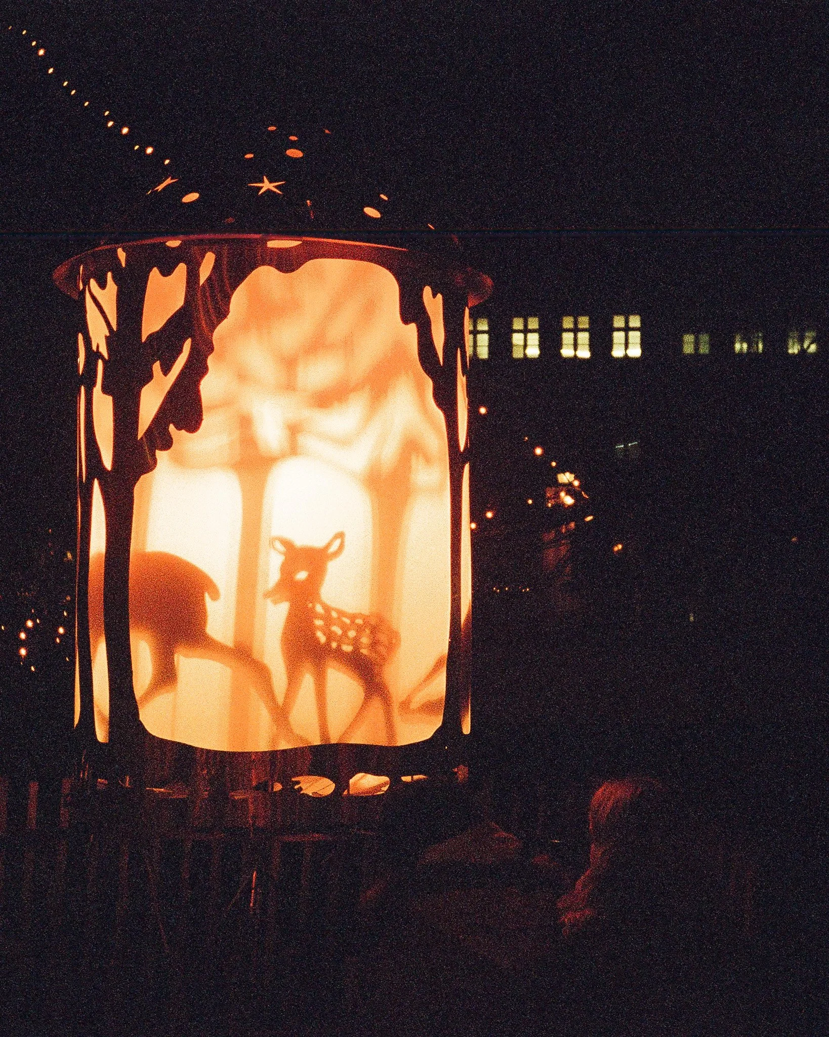 Silhouette of a paper lantern with deer and forest scene cutouts, glowing in a dark setting.