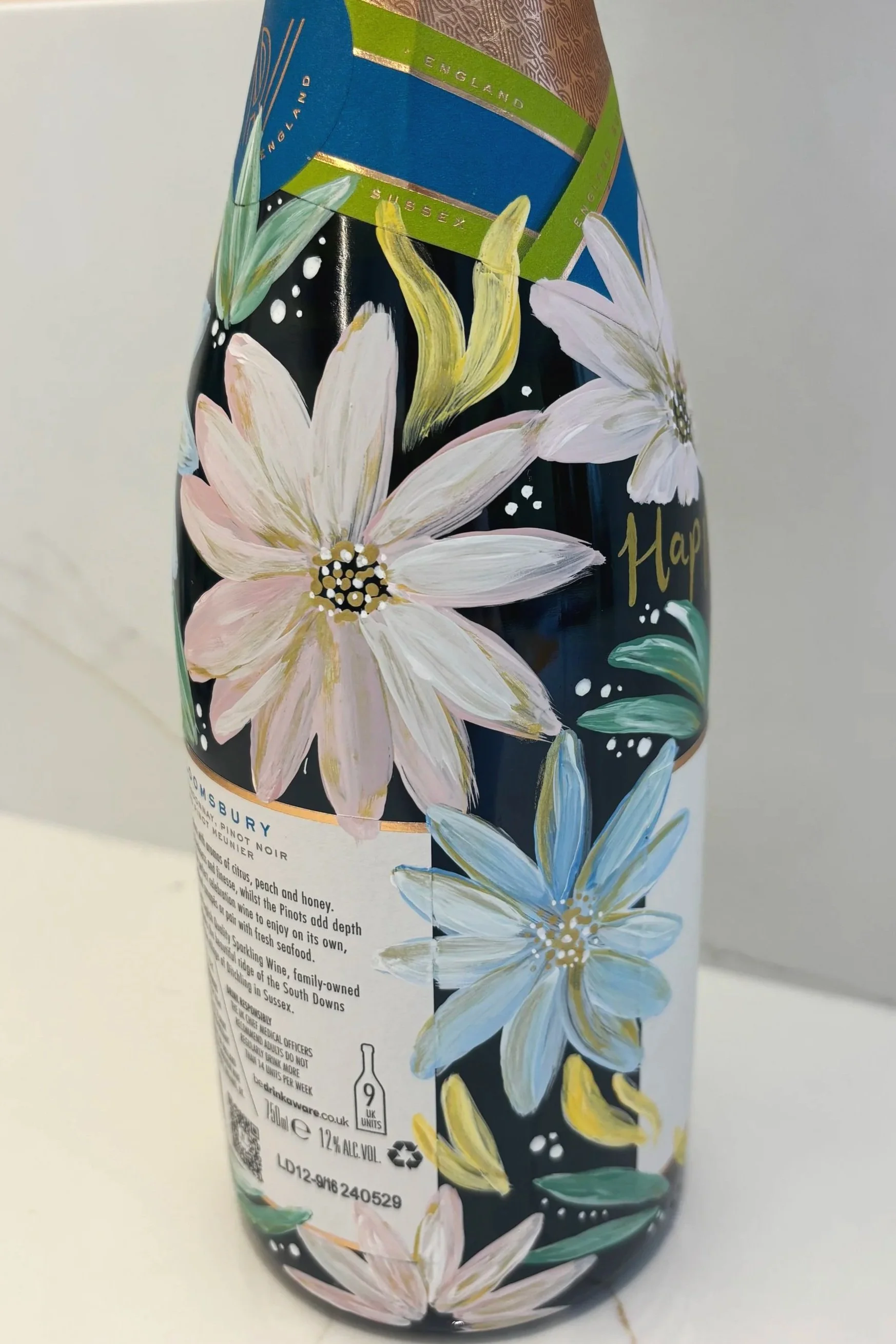 Hand painted bottle of English sparkling wine, painted in cool floral tones of green and blue. Painted champagne bottle. By Minutes Illustration