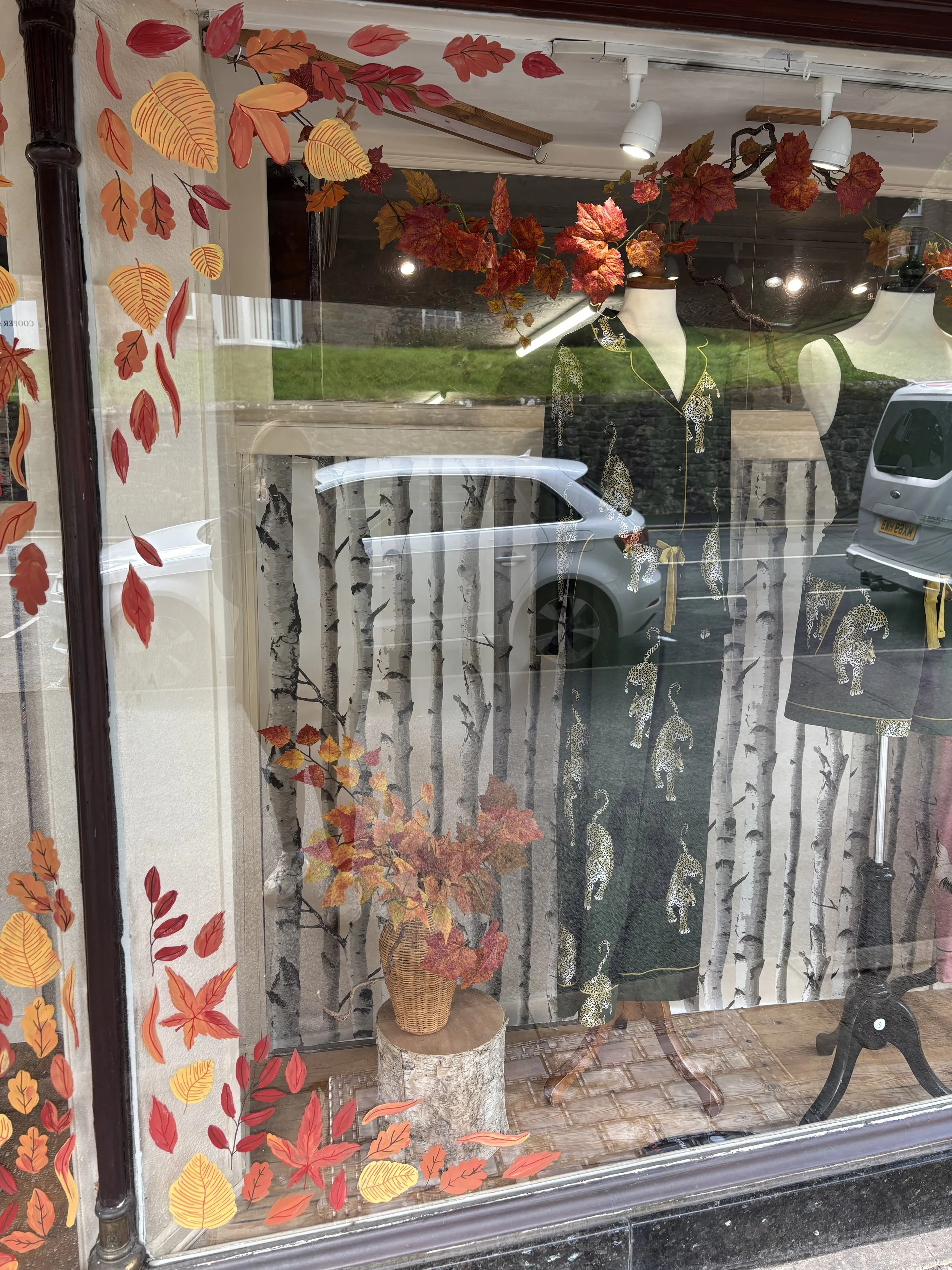 Autumn artwork painted on the front of a shop window. Different types of autumn leaves are fluttering around the windows, hand painted by By Minutes Illustration. 