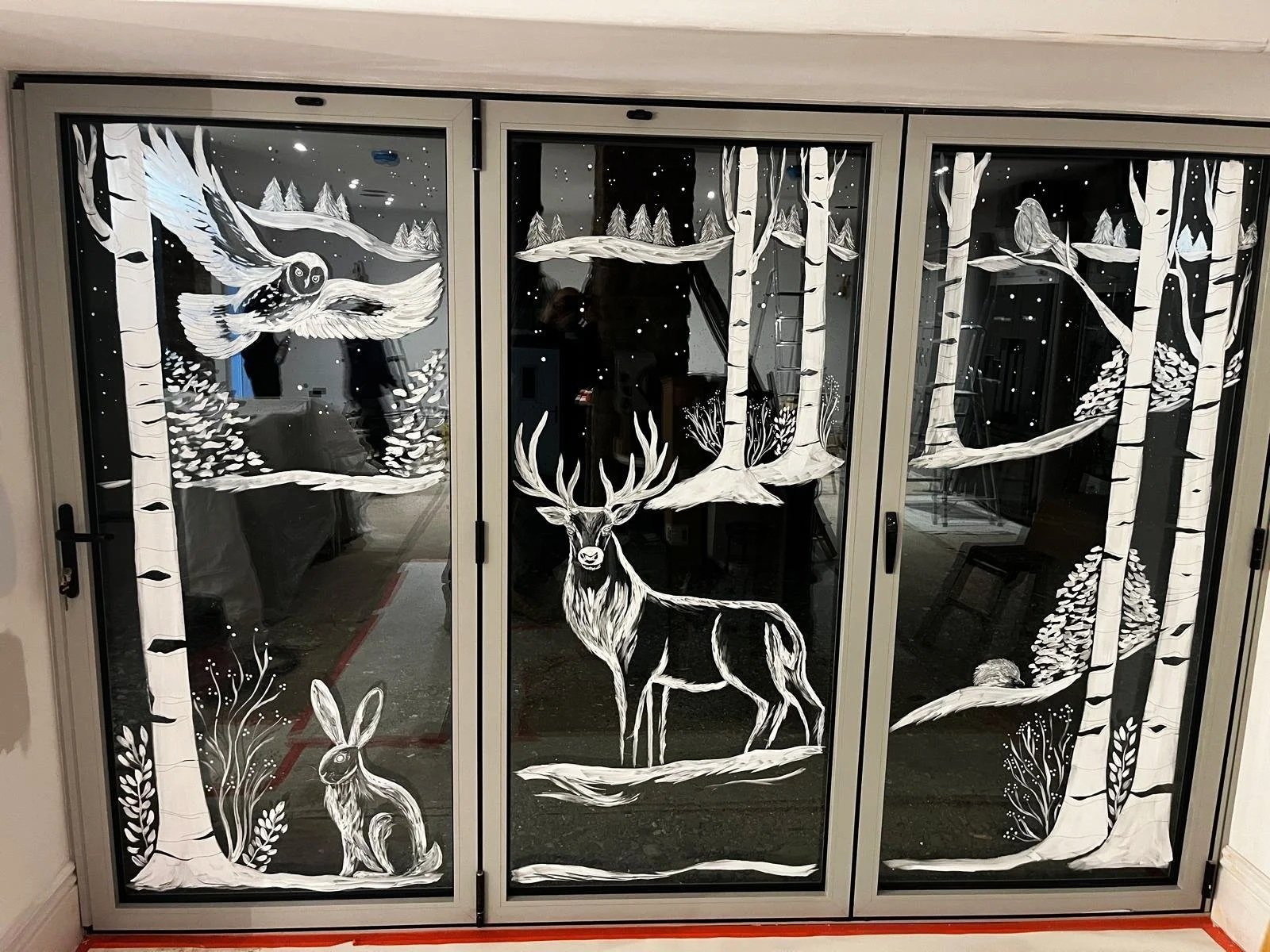 Christmas hand painted window of a winter snow scene with a stag, owl and rabbit. Hand painted window art. Hand painted window display. 