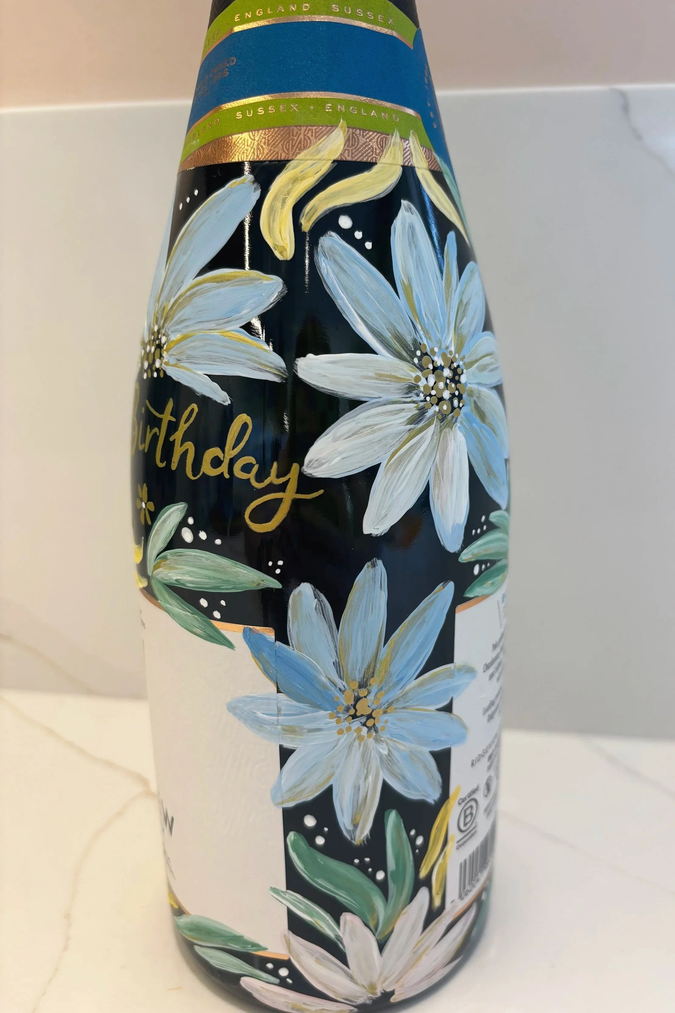 Hand painted bottle of English sparkling wine, painted in cool floral tones of green and blue. Painted champagne bottle. By Minutes Illustration