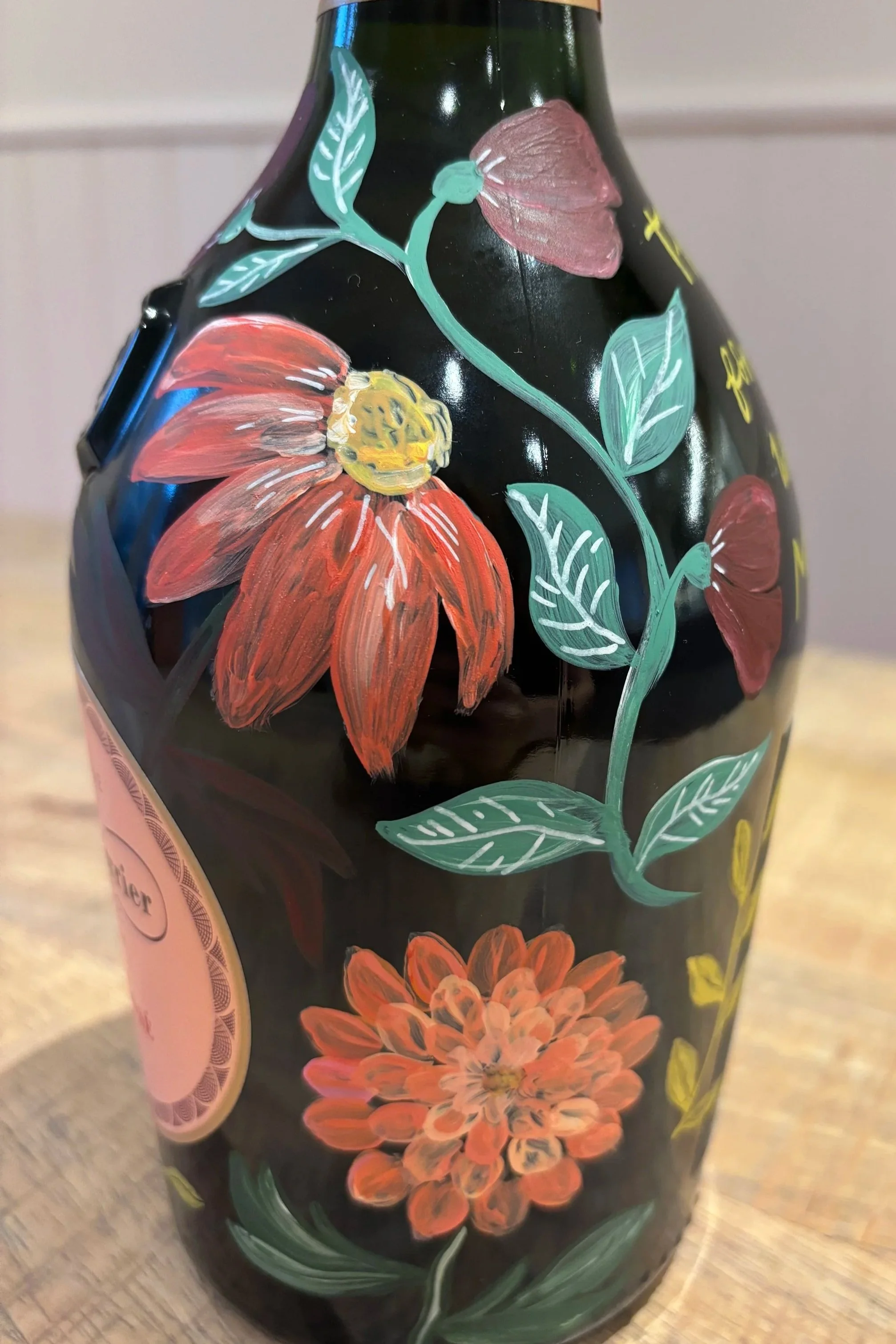 Hand painted bottle of champagne painted with pink flowers and orange flowers.