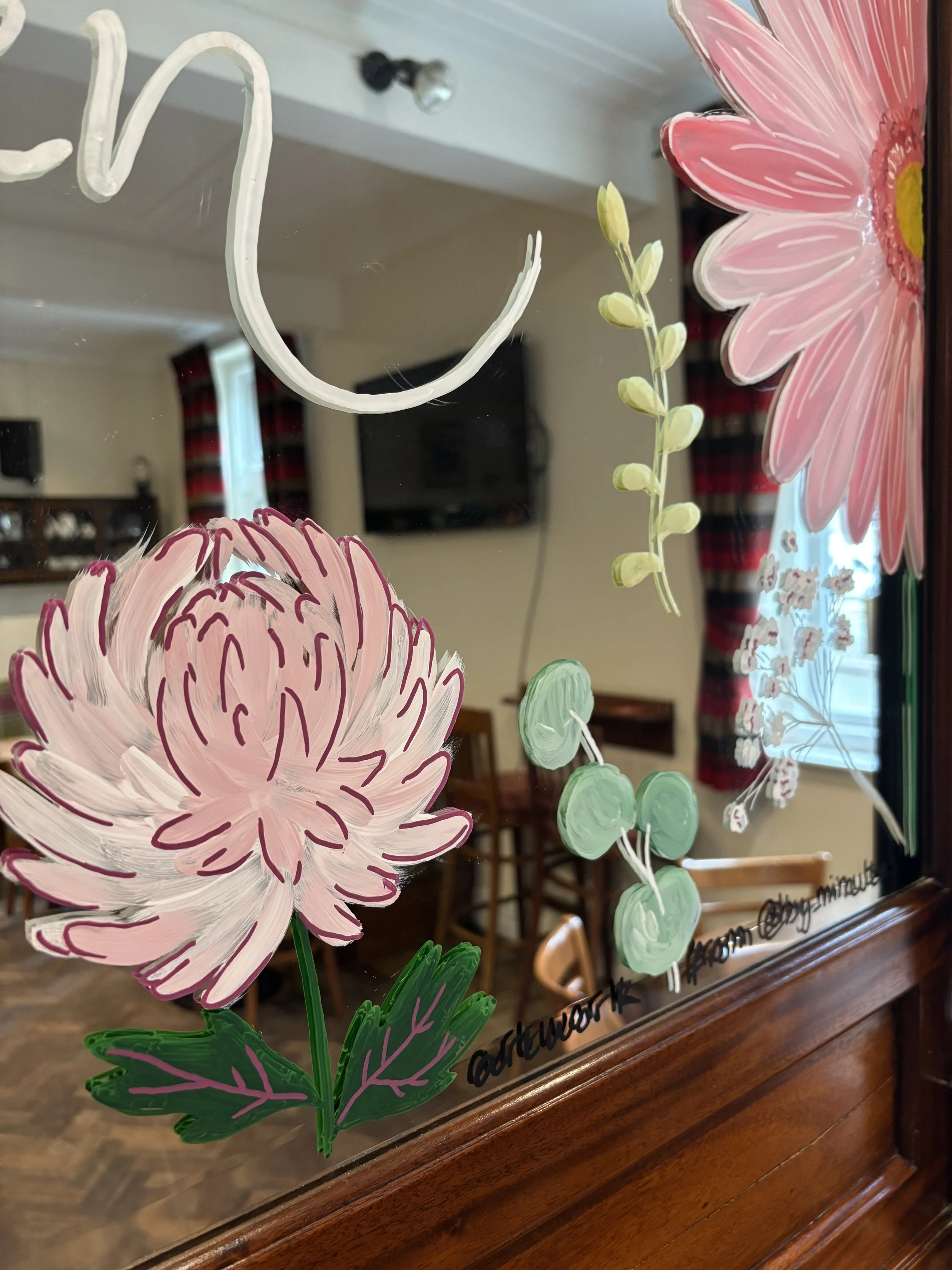 Hand painted glass window with painted pink and white flowers, green leaves, and small green buds, with a room visible in the background.