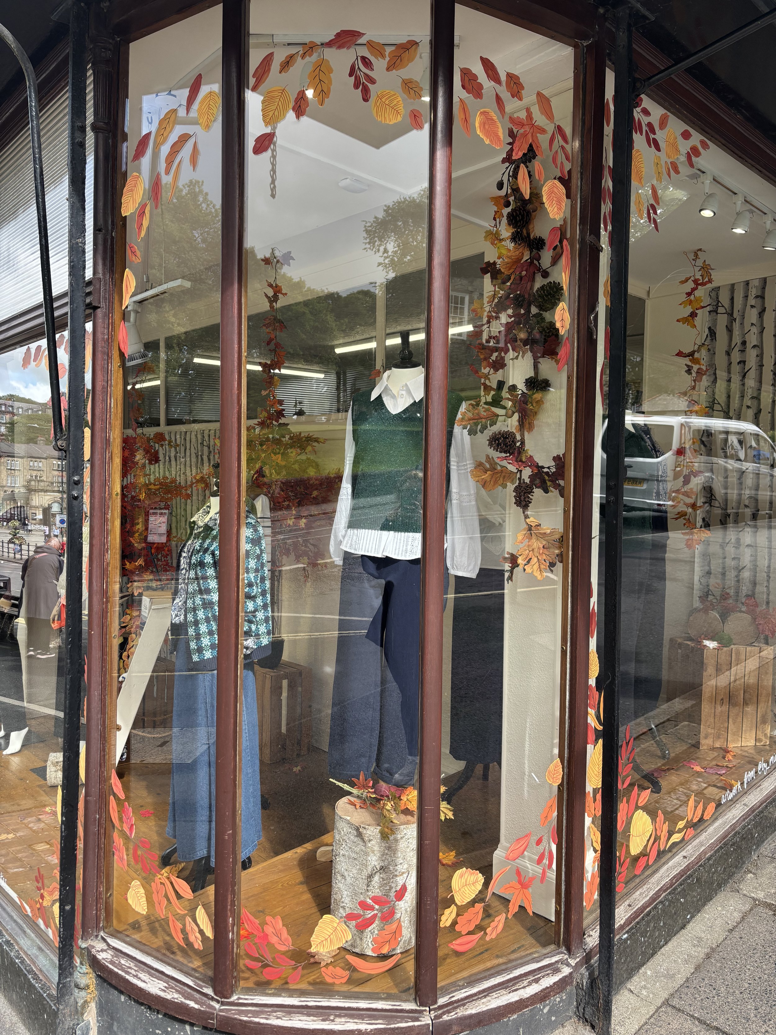 Hand painted window illustrator painting autumns leaves on a clothes shop window. Various autumn leaves around the windows. Window painting. 
